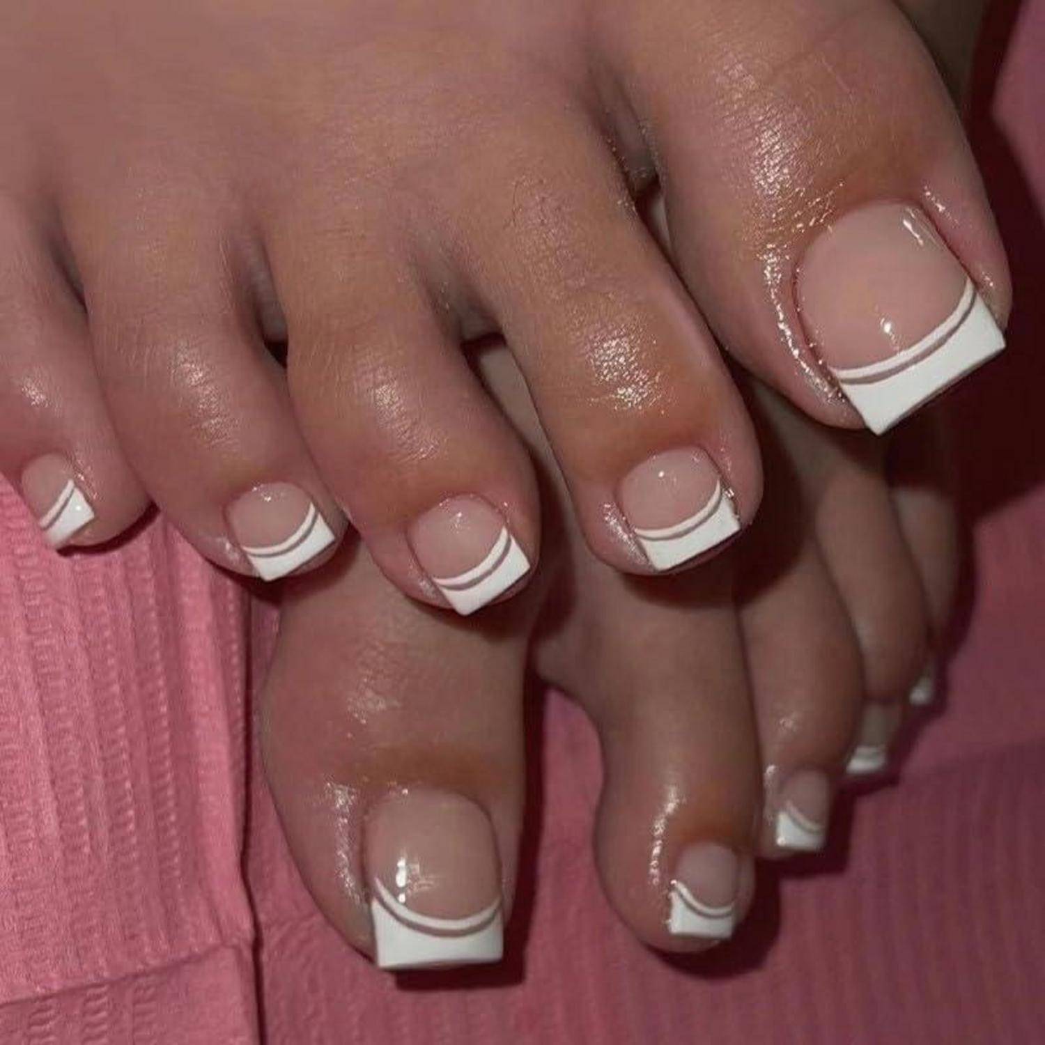 Nahaufnahme von Händen und Füßen mit nacktem Nagellack und weißer French-Manicure-Nagelkunst, ruhend auf einer rosa gerippten Oberfläche.