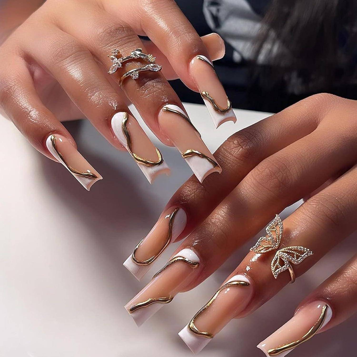 Nahaufnahme von Händen mit langen weiß-goldenen French-Nails, verziert mit dekorativen Schmetterlings- und Schmuckringen.