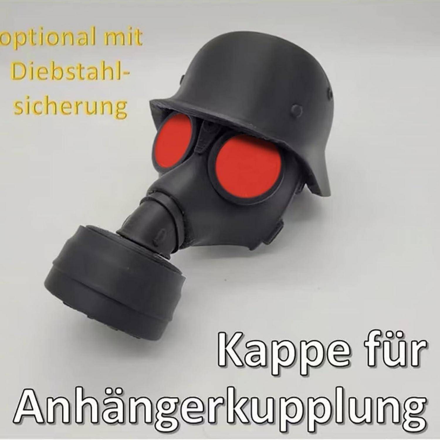Schwarze Gasmasken-ähnliche Abdeckung für Anhängerkupplung mit roten Augenlinsenelementen; deutscher Text besagt „optional mit Diebstahlschutz