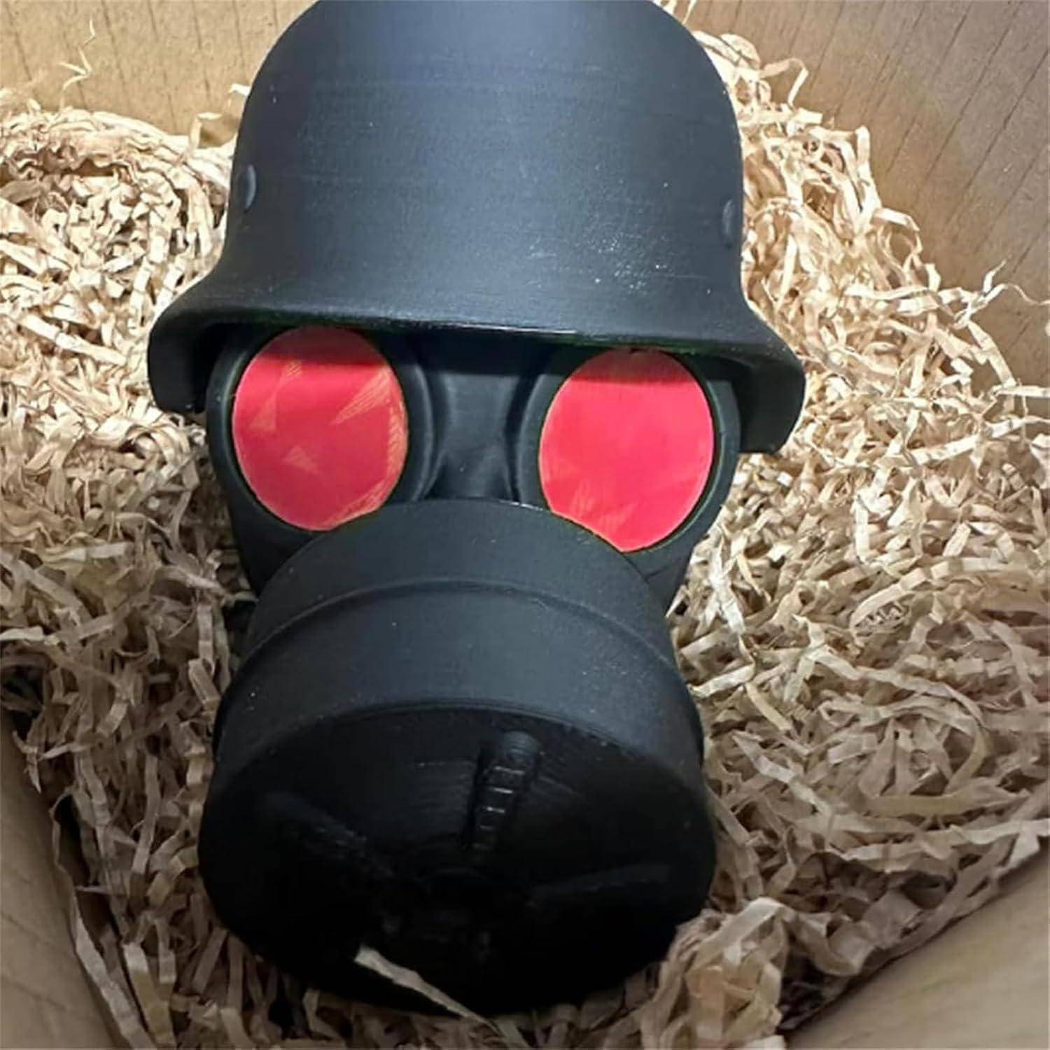 Schwarze Gasmaske mit roten Gläsern, eingebettet in zerkleinertes Packpapier in einem Karton.