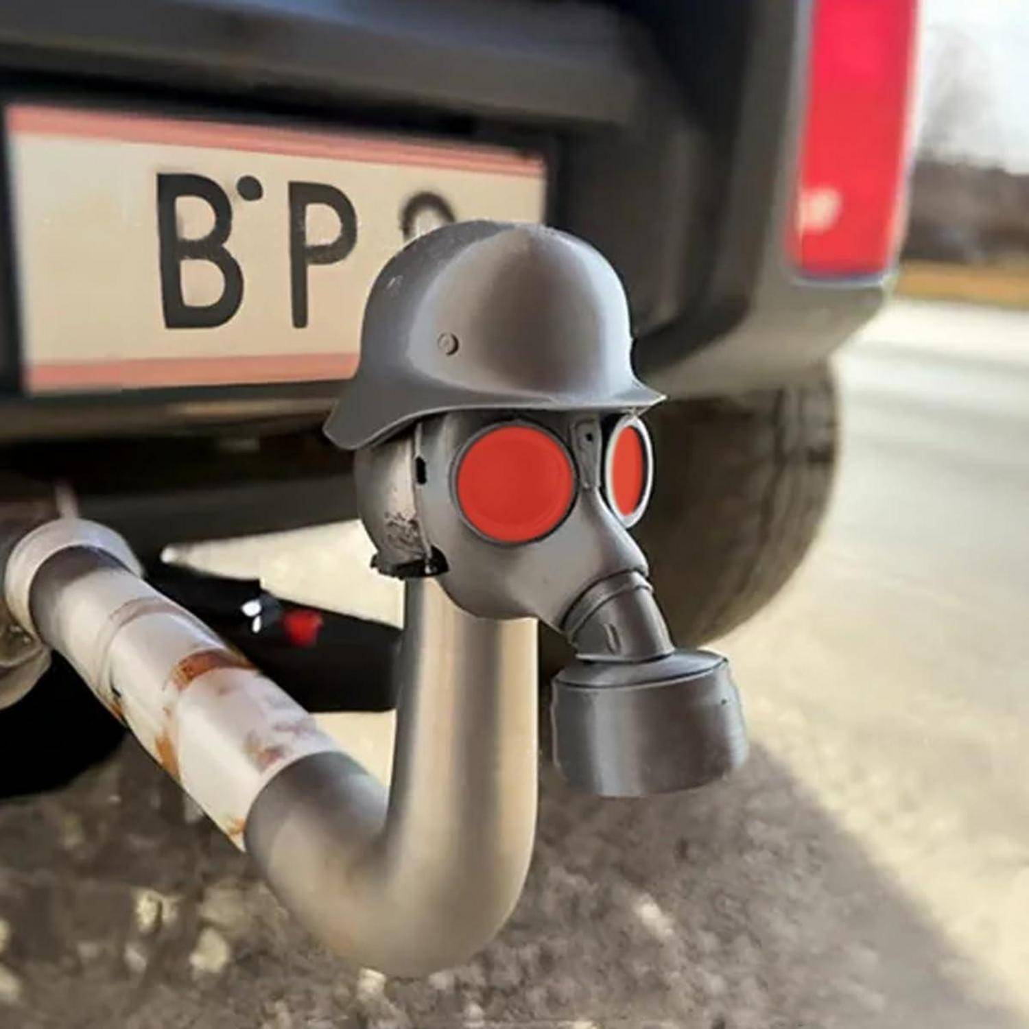 Ein humorvolles Heck-Autoaccessoire in Form eines Soldaten mit Gasmaske und Helm, das an dem Auspuffrohr befestigt ist, mit einem teilweise sichtbaren Nummernschild dahinter.