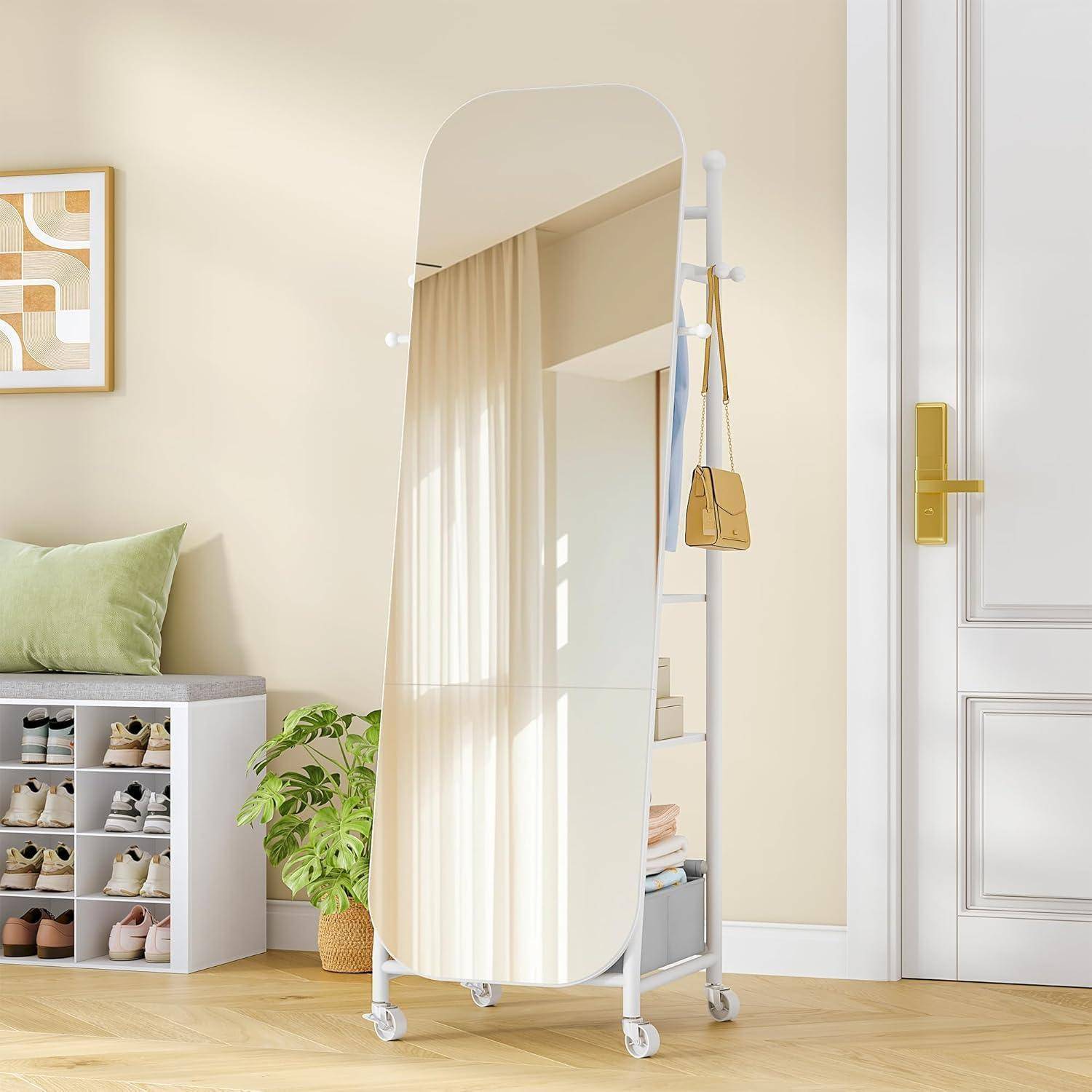 Ein freistehendes, bodenlanger Spiegel auf Rollen in einem hellen Schlafzimmer, mit Schuhen, einer Pflanze und einer Bank mit Kissen in der Nähe.