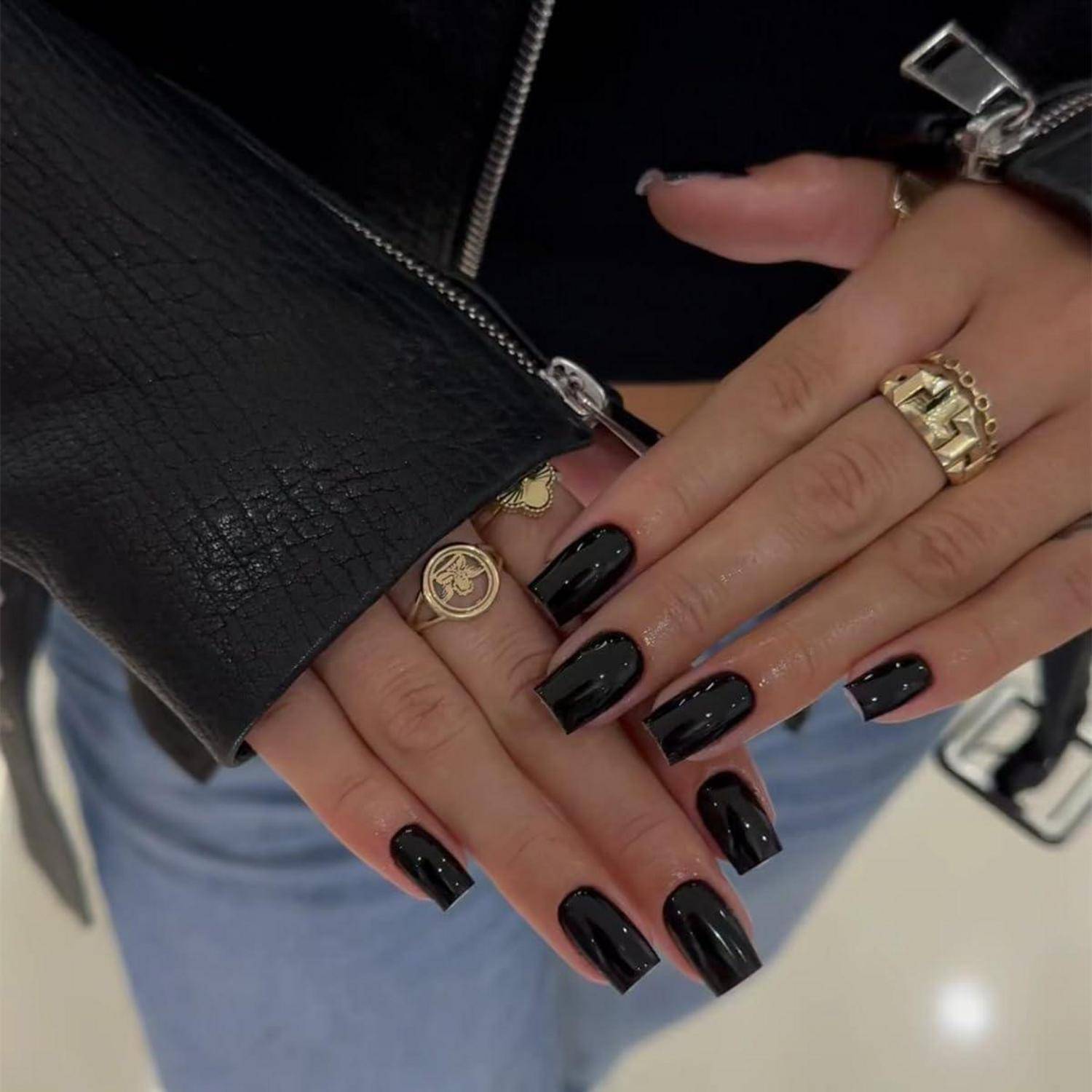 Nahaufnahme von zwei Händen mit glänzend schwarzer Maniküre und goldenen Ringen, eine Hand ruht auf einer schwarzen Ledertasche über hellblauen Jeans.