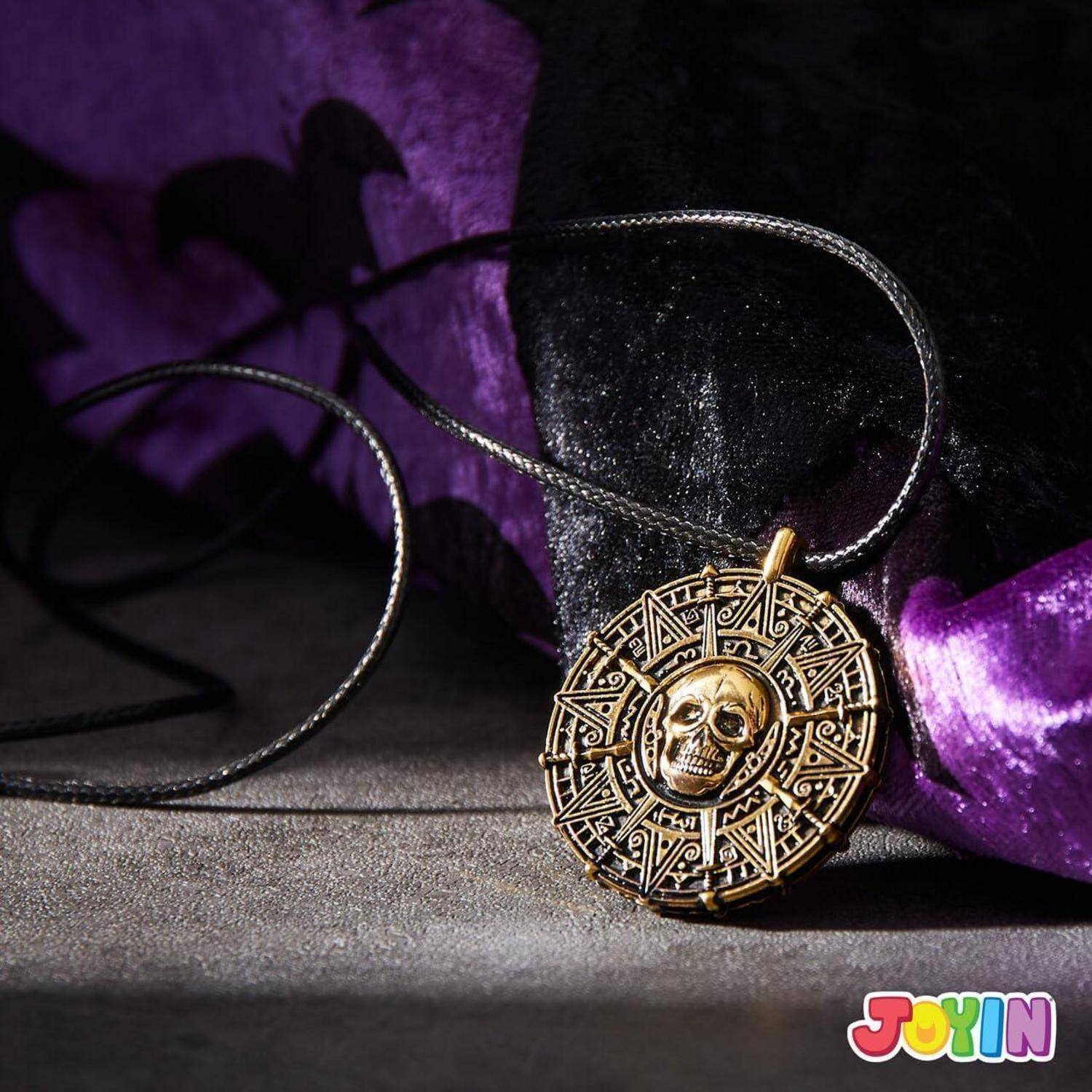 Goldschädel-Medaillon-Anhänger an einer schwarzen Schnur, liegend auf violettem Stoff und einer dunklen Oberfläche.