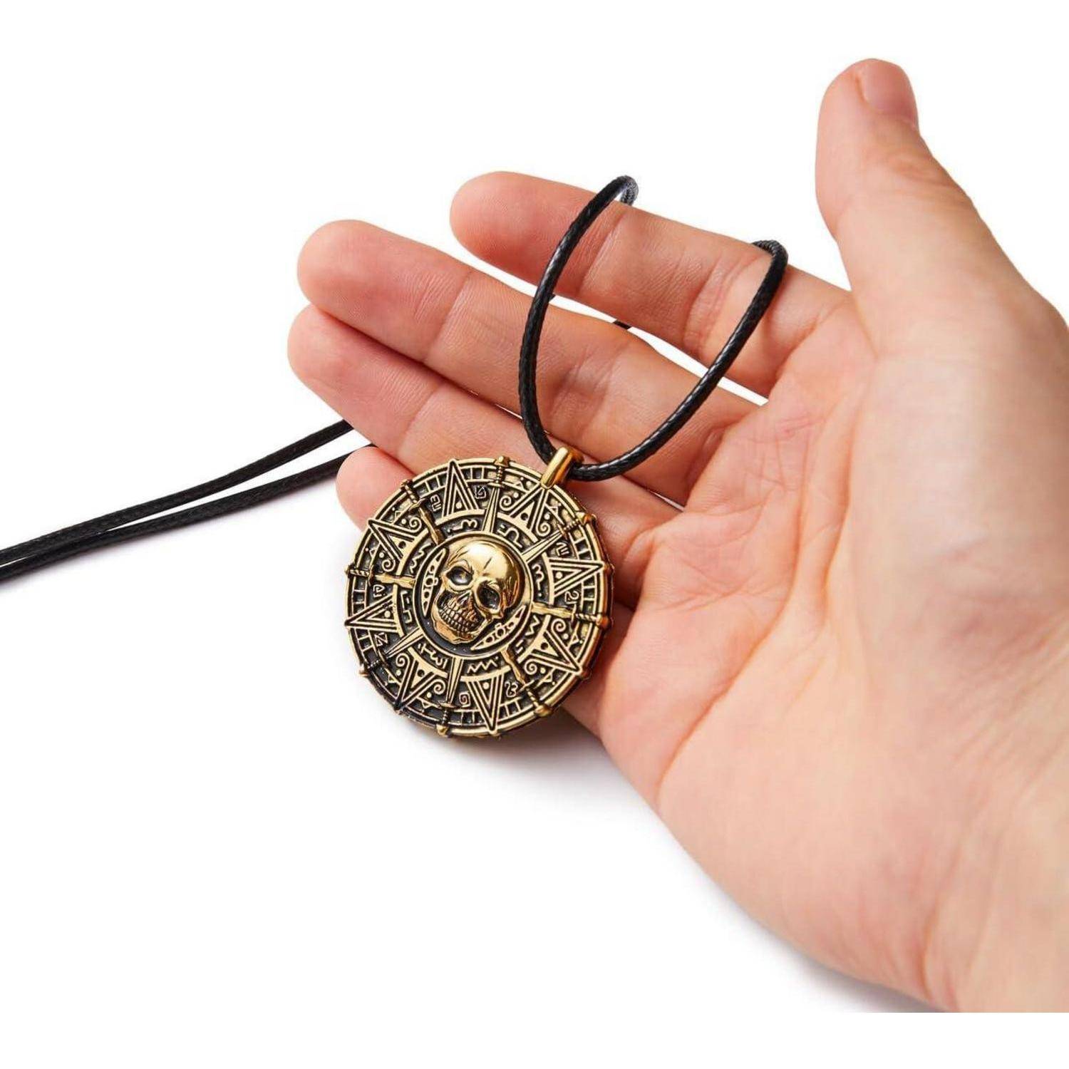 Hand, die eine schwarze Kordelkette mit einem aufwendigen runden goldenen Anhänger mit Totenkopf-Design auf weißem Hintergrund hält.
