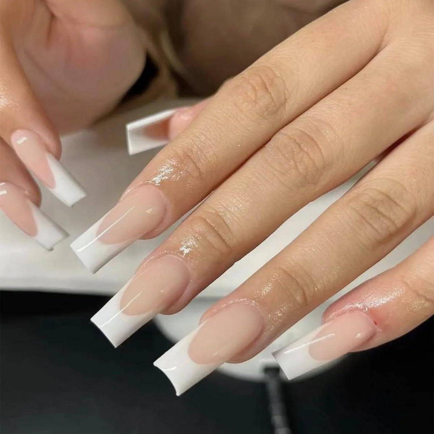 Nahaufnahme von Händen mit langen quadratischen French-Manicure-Nägeln in Nude-Rosa und Weiß.