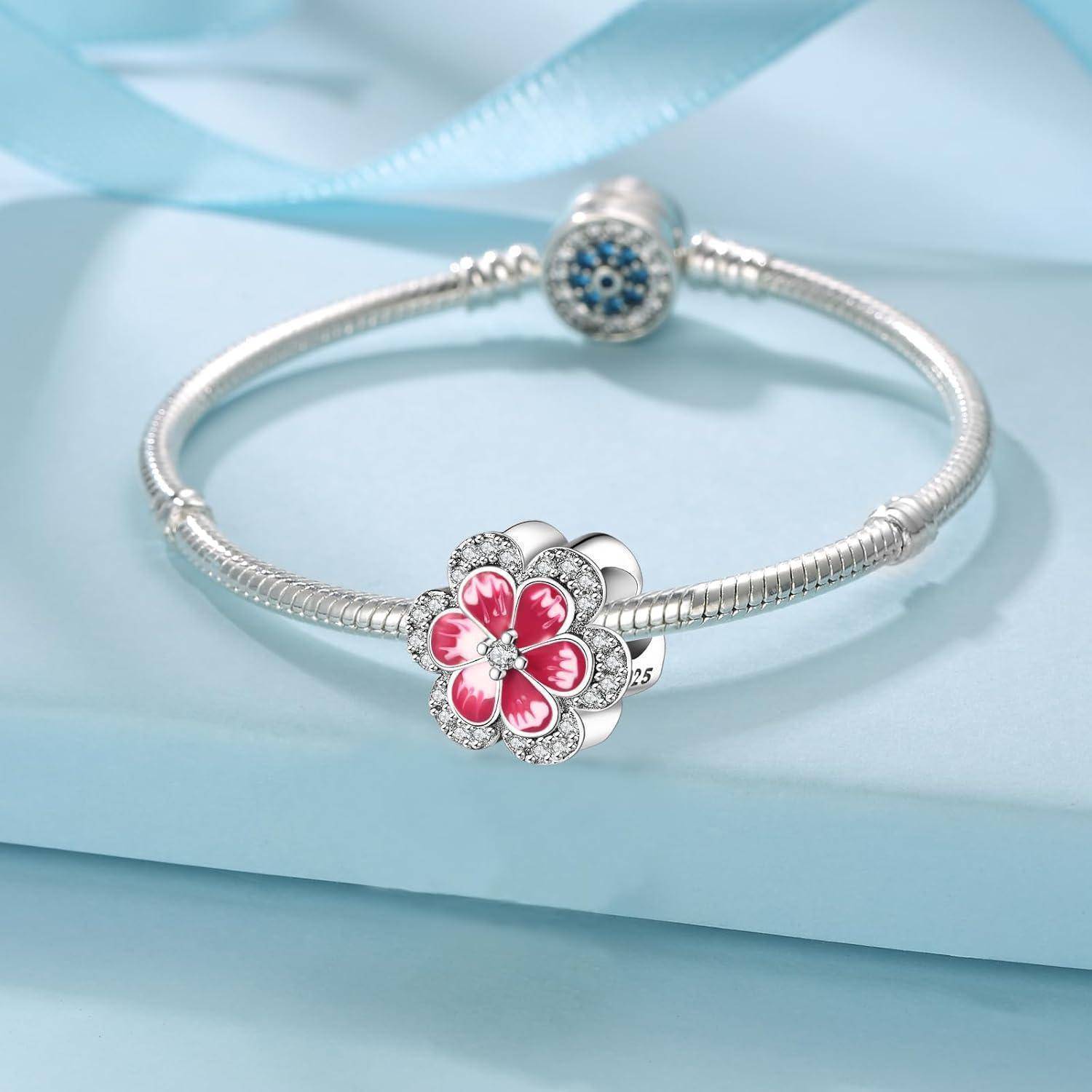 Silbernes Charm-Armband mit einer rosa Blumenperle und einer blauen Pavé-Perle auf hellblauem Hintergrund.
