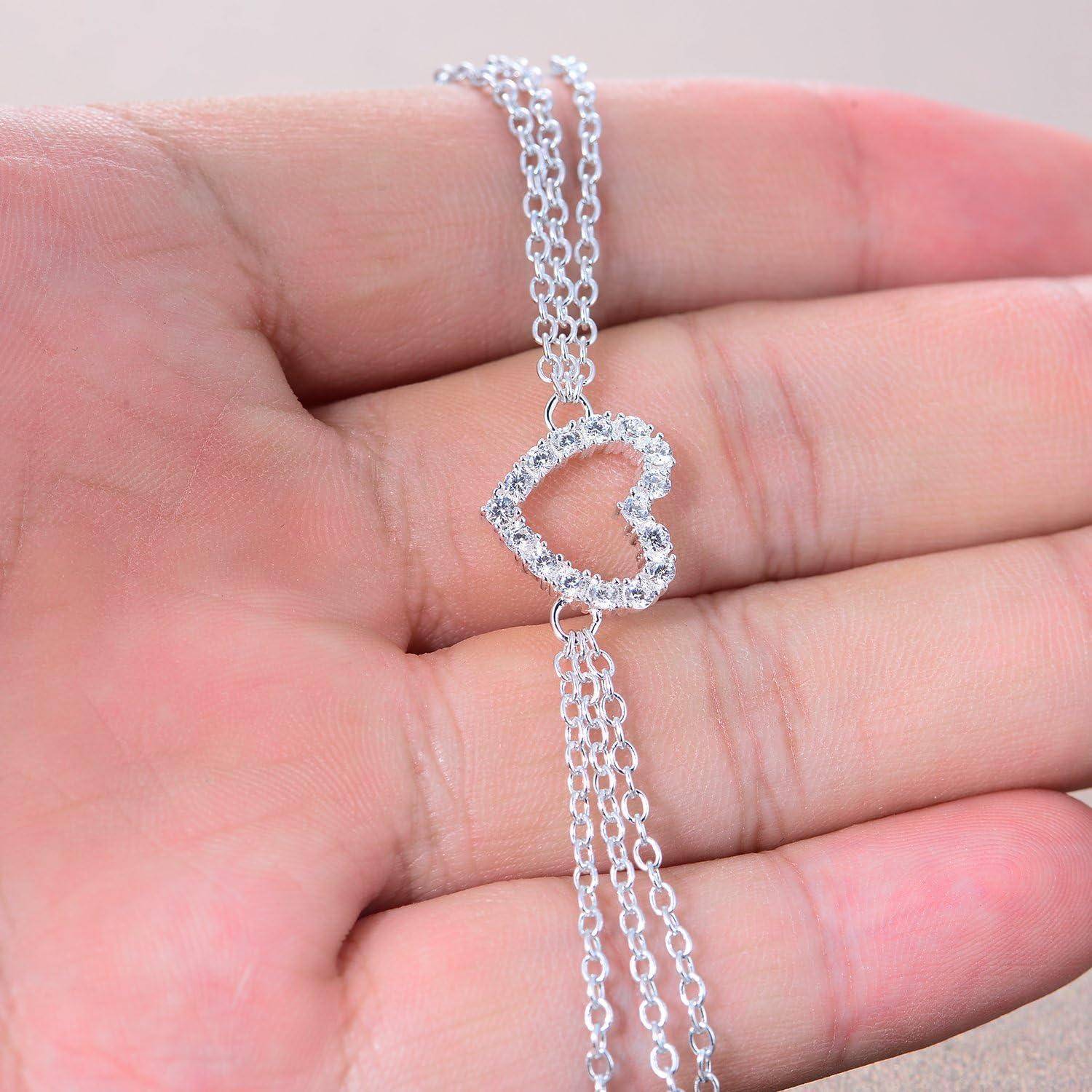 Silbernes Armband mit einem offenen Herzanhänger und baumelnden Kettequasten, das auf der Handfläche einer Person ruht.