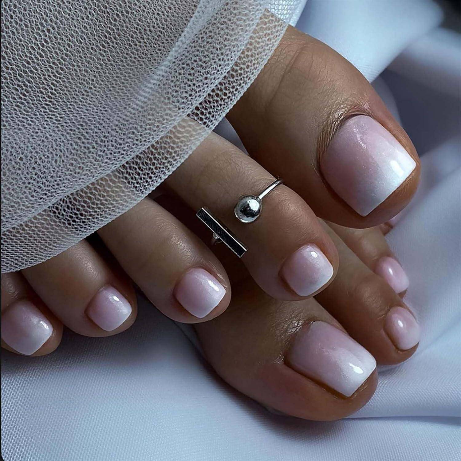 Nahaufnahme von gepflegten Zehen mit hellem rosa glänzendem Nagellack und silbernen Zehenringen, ruhend auf weißem Stoff mit durchsichtigem Mesh-Stoff darüber drapiert.