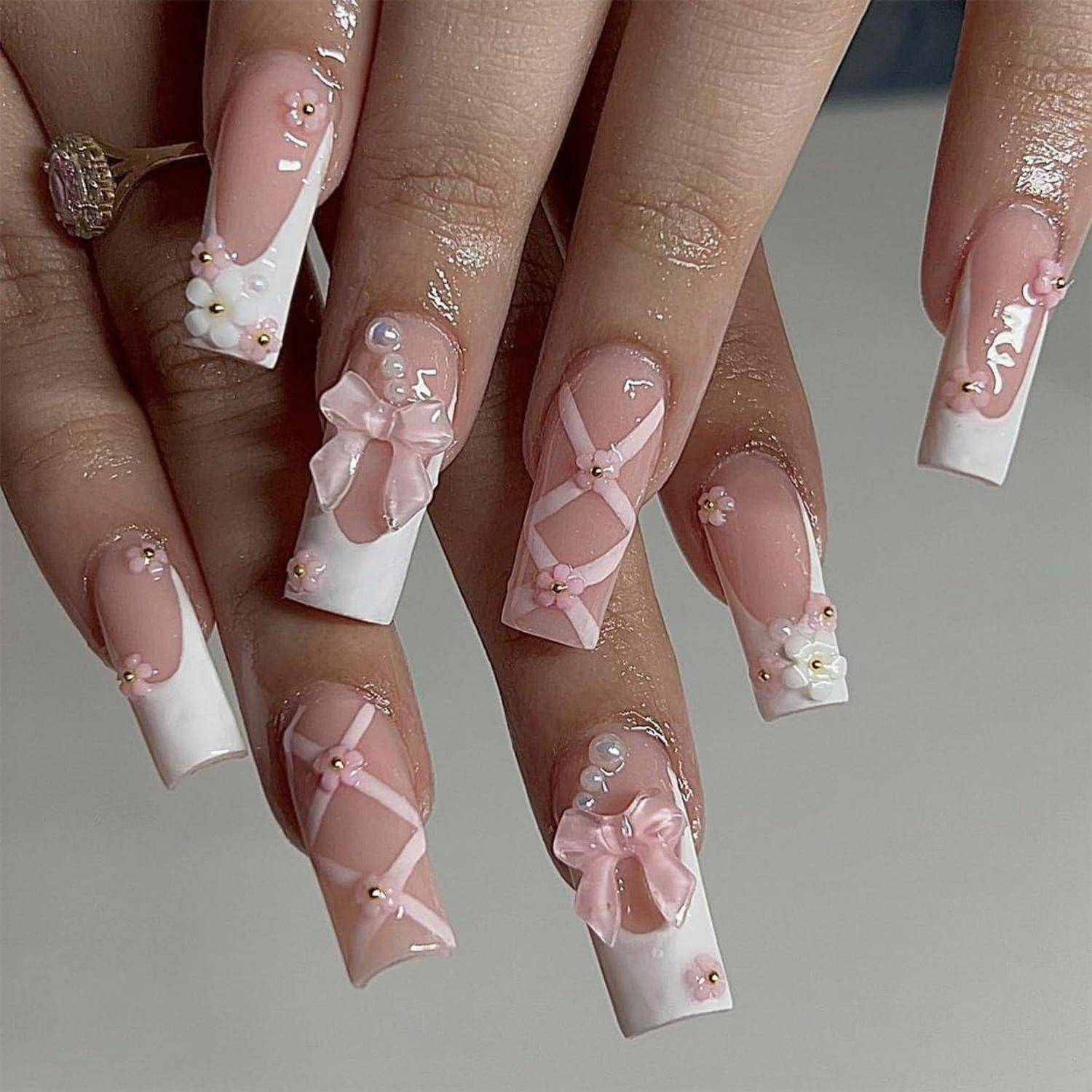 Nahaufnahme von Händen mit langen rosa und weißen Acrylnägeln, verziert mit 3D-Schleifen, Perlen und floralen Akzenten.