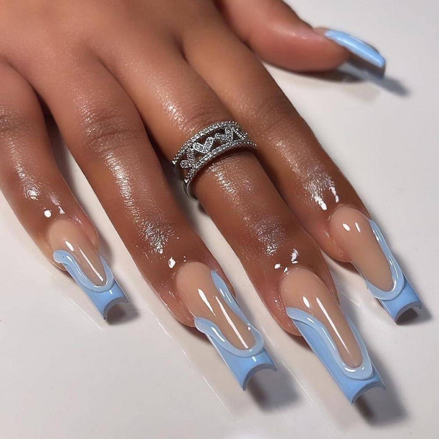 Nahaufnahme einer Hand mit langen Acryl-Nägeln in Blau-und-Nude-Ombré und einem silbernen geometrischen Ring.