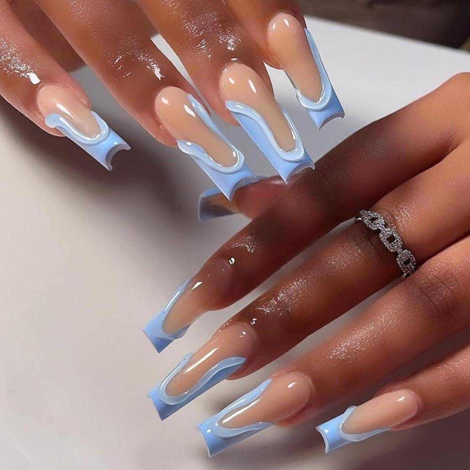 Nahaufnahme von Händen mit langen, nudes und hellblauen French-Manicure-Nägeln, die ein glänzendes Nageldesign und einen silbernen Ring zeigen.