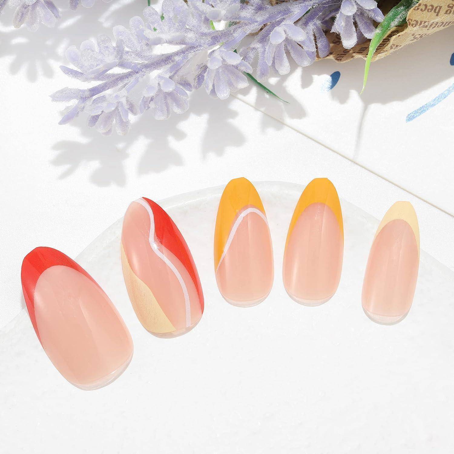 Fünf künstliche Nagelspitzen in Nude-, Pfirsich-, Rot- und Gelbdesigns werden auf einer weißen Oberfläche präsentiert.