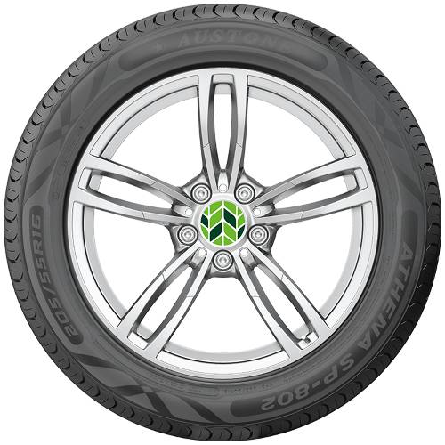 Nahaufnahme eines Autoreifens und silbernen Leichtmetallrads mit grünem Mittellogo, frontal vor schwarzem Hintergrund fotografiert.