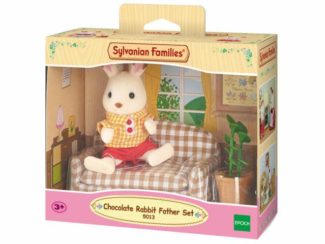 Sylvanian Families 'Schokoladenkaninchen-Papa-Set' Spielzeugschachtel zeigt eine weiße Kaninchenfigur, die auf einem Sofa in einer Puppenhaus-Wohnzimmerszene sitzt.