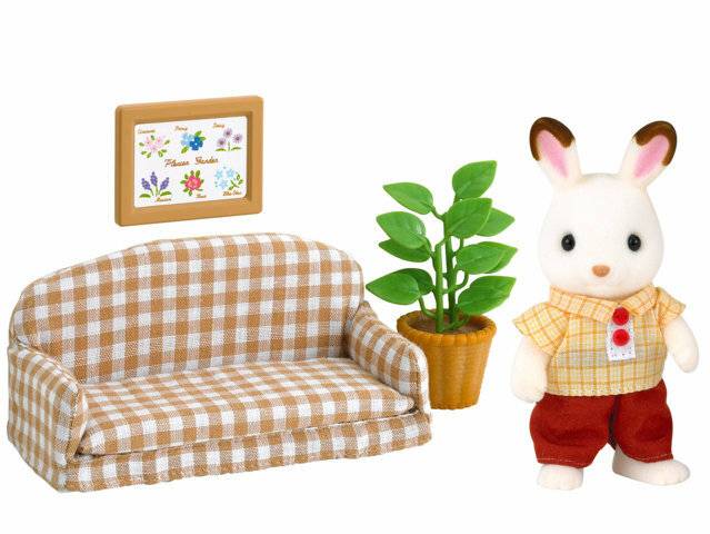 Kaninchenfigur neben einem karierten Sofa, einer Topfpflanze und einem gerahmten Wandbild, das einer Miniatur-Wohnzimmerszene ähnelt.