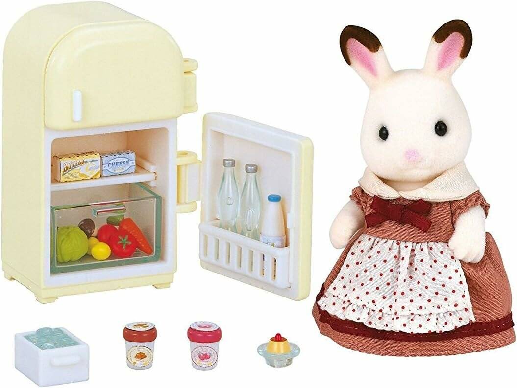 Eine Spielzeugkaninchenfigur in einem Kleid steht neben einem offenen Miniaturkühlschrank mit Lebensmitteln und kleinen Accessoires, die darin und darunter ausgestellt sind.