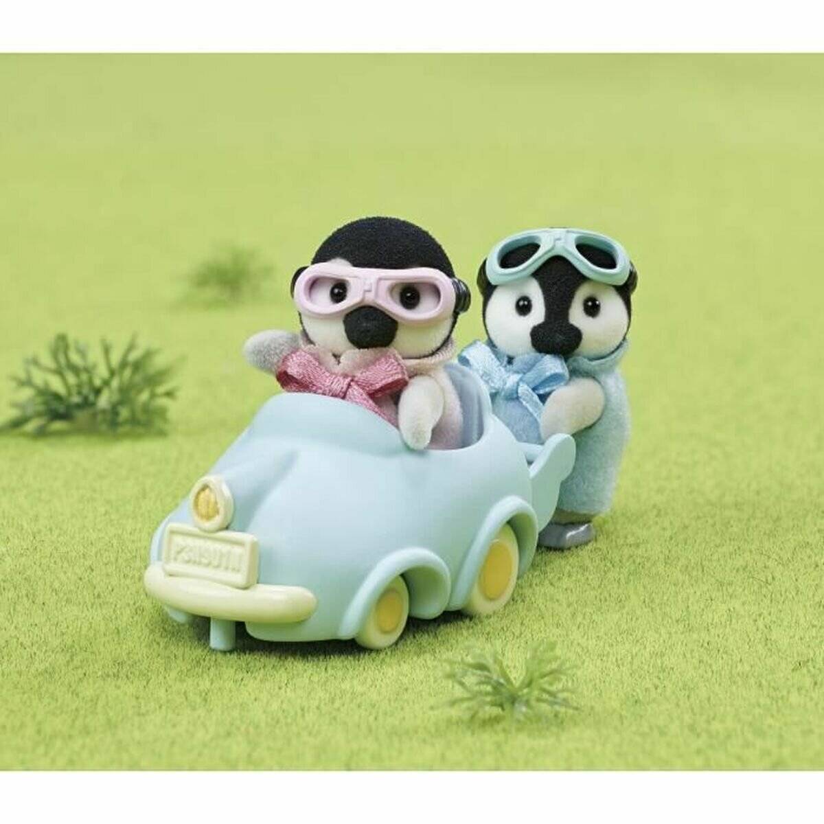 Zwei Spielzeugtiere mit Schutzbrille fahren in einem kleinen hellblauen Auto auf grünem Gras, wobei das zweite von hinten anschiebt.