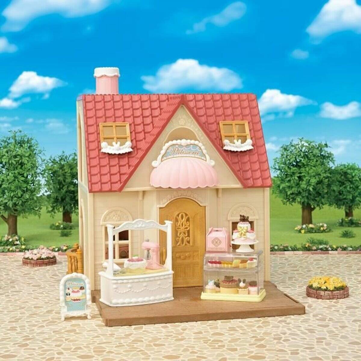 Miniatur-Bäckerei-Spielhaus mit rotem Dach, das Kuchen und Gebäck draußen auf einer hölzernen Veranda in einer Gartenumgebung ausstellt.