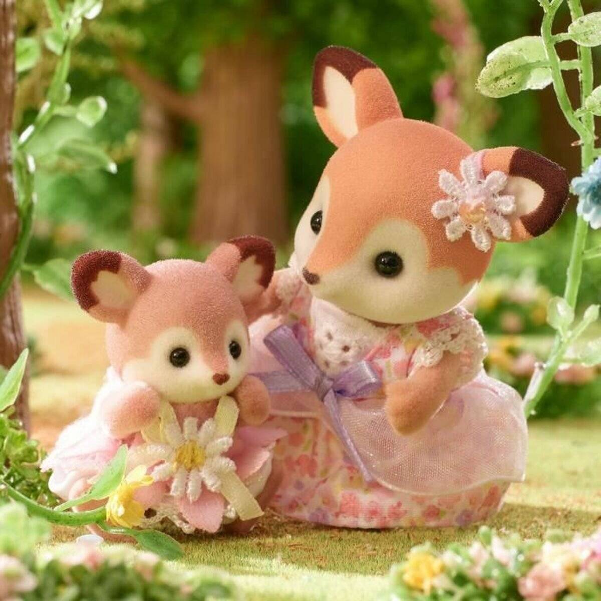 Zwei blumengeschmückte Spielzeug-Hirsche stehen in einem Miniatur-Garten, einer größer mit einer Schleife und einer Blumen-Haarspange, einer kleinerer mit einem Gänseblümchen in der Hand.