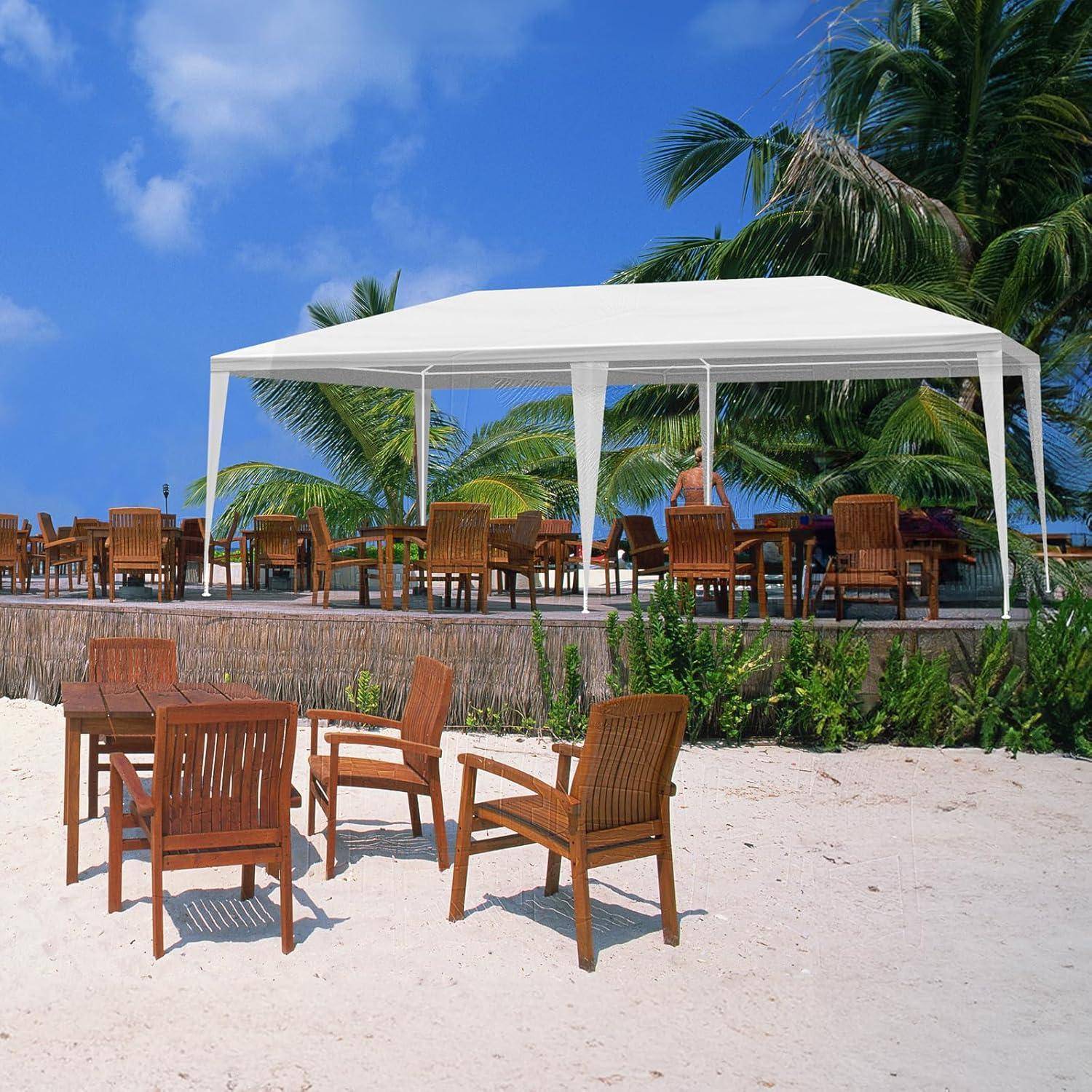 Strandlounge-Bereich mit Holztischen und Stühlen unter einem weißen Baldachin, Palmen und blauem Himmel im Hintergrund.