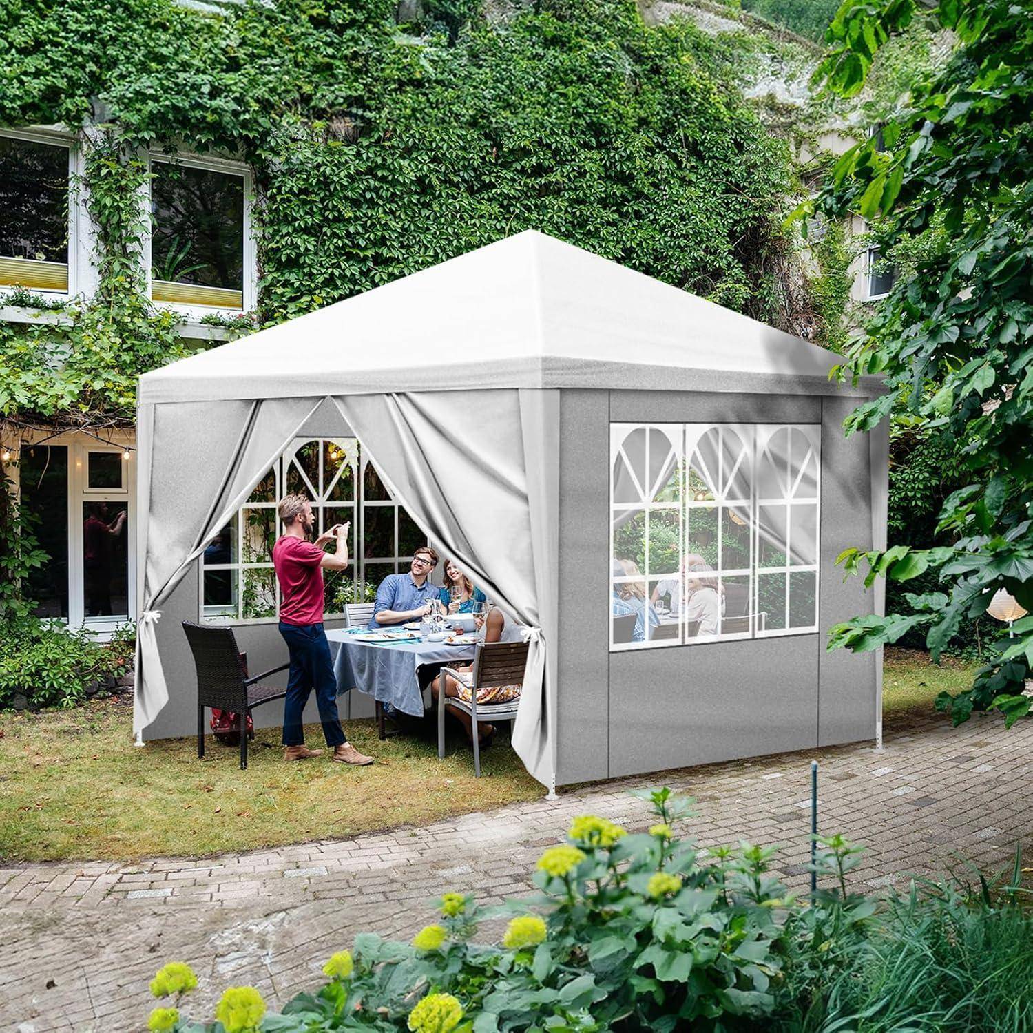 Essensszene im Freien in einem grauen Pop-up-Pavillonzelt in einem grünen Innenhof, mit Personen, die an einem Tisch sitzen, und einer anderen Person, die ein Foto macht.