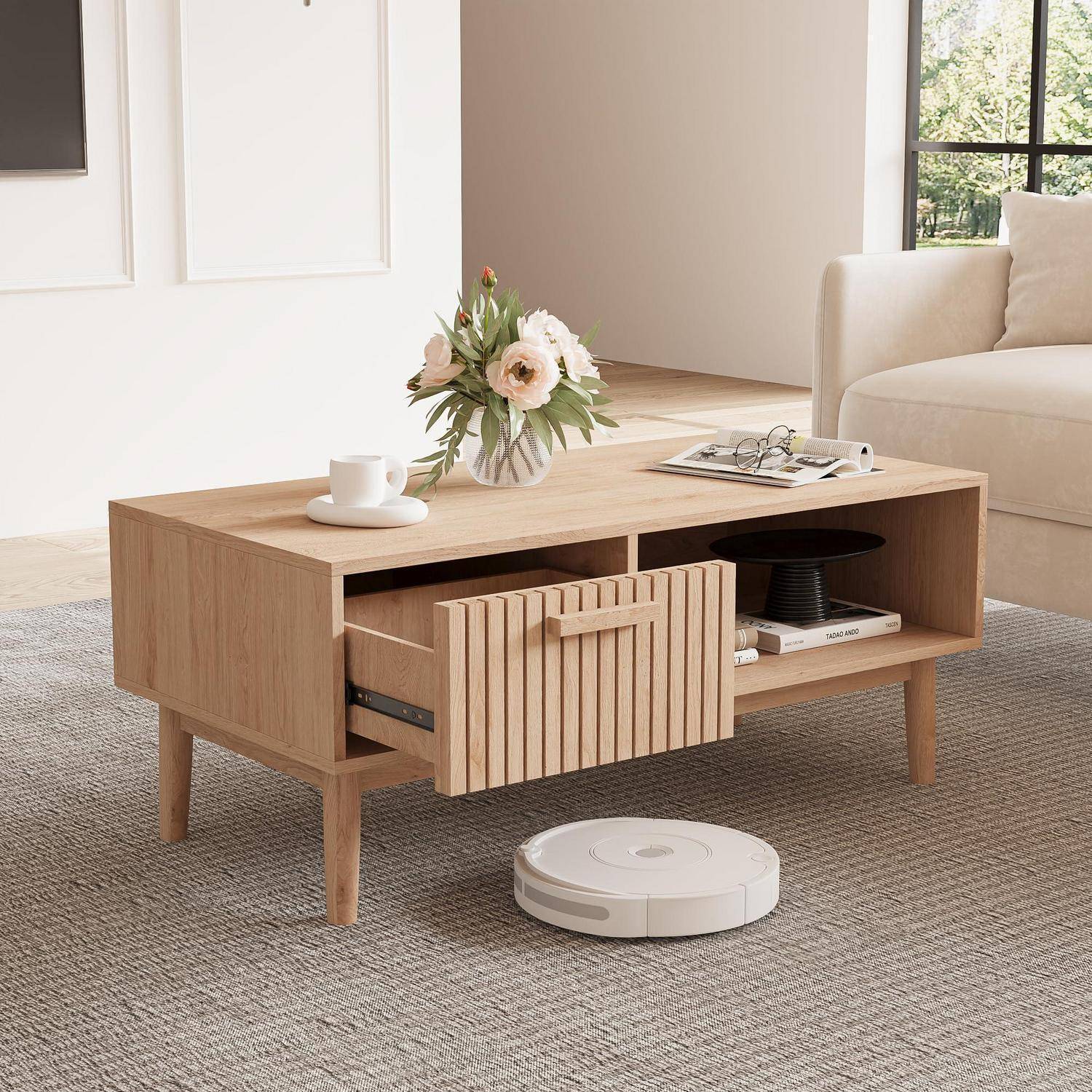Holztisch mit Lamellenschublade zum Herausziehen und offenen Regalen in einem hellen Wohnzimmer, mit Blumen, einer Tasse und einem Staubsaugroboter darunter.