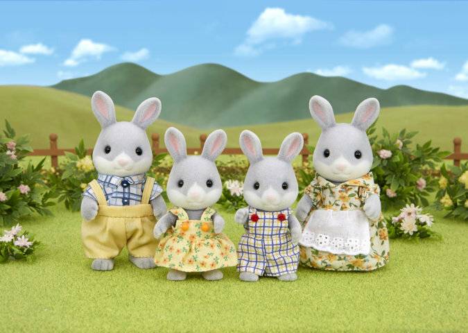 Vier gefüllte Häschenfiguren in Pastelloutfits stehen zusammen im Freien auf einer grünen Wiese mit Blumen, Hügeln und blauem Himmel.