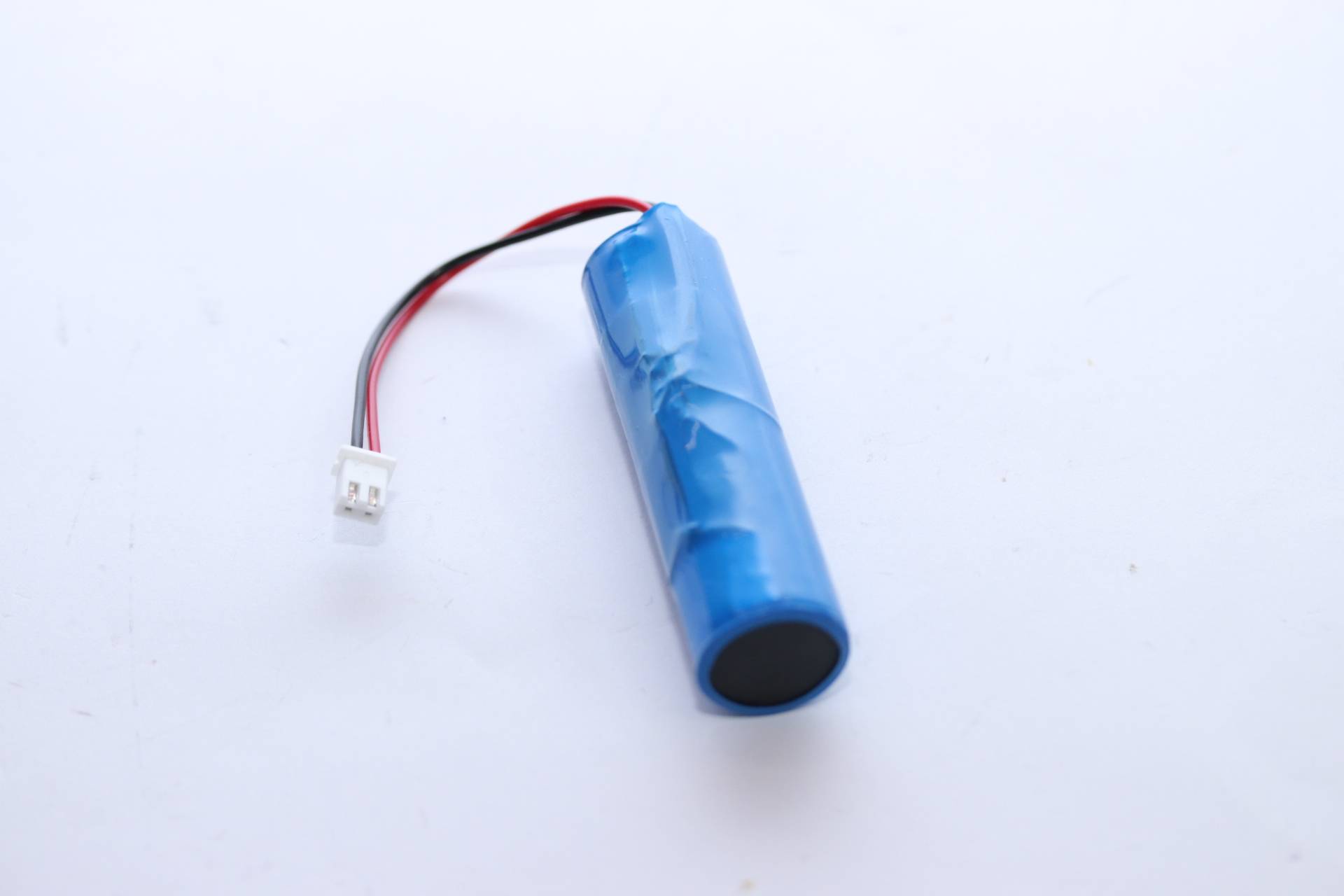 Blauer zylindrischer Akkupack mit roten und schwarzen Drähten, die in einem kleinen weißen Stecker enden.