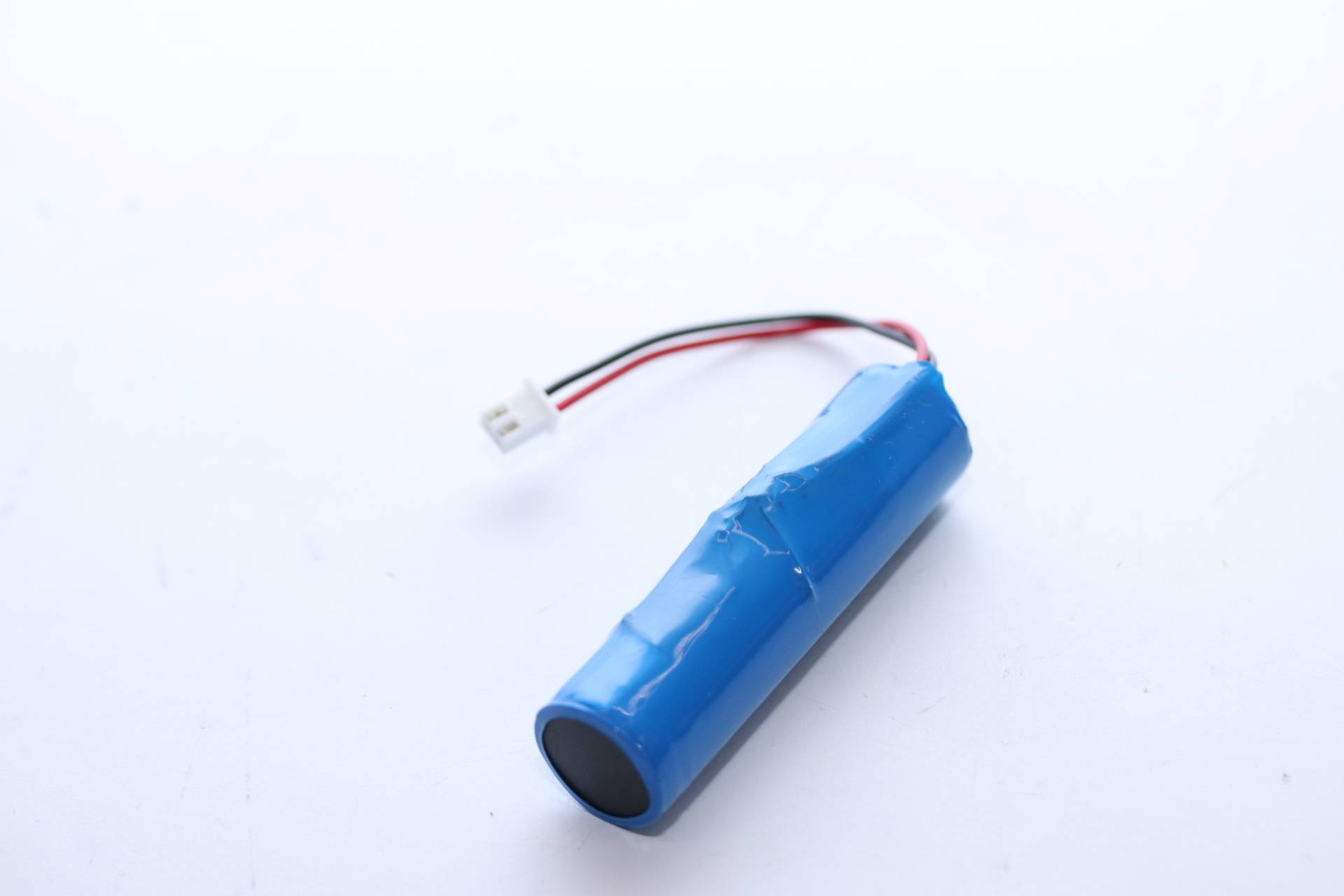 Blauer zylindrischer Batteriepack mit roten und schwarzen Drähten und einem kleinen weißen Anschluss auf einfachem weißem Hintergrund.