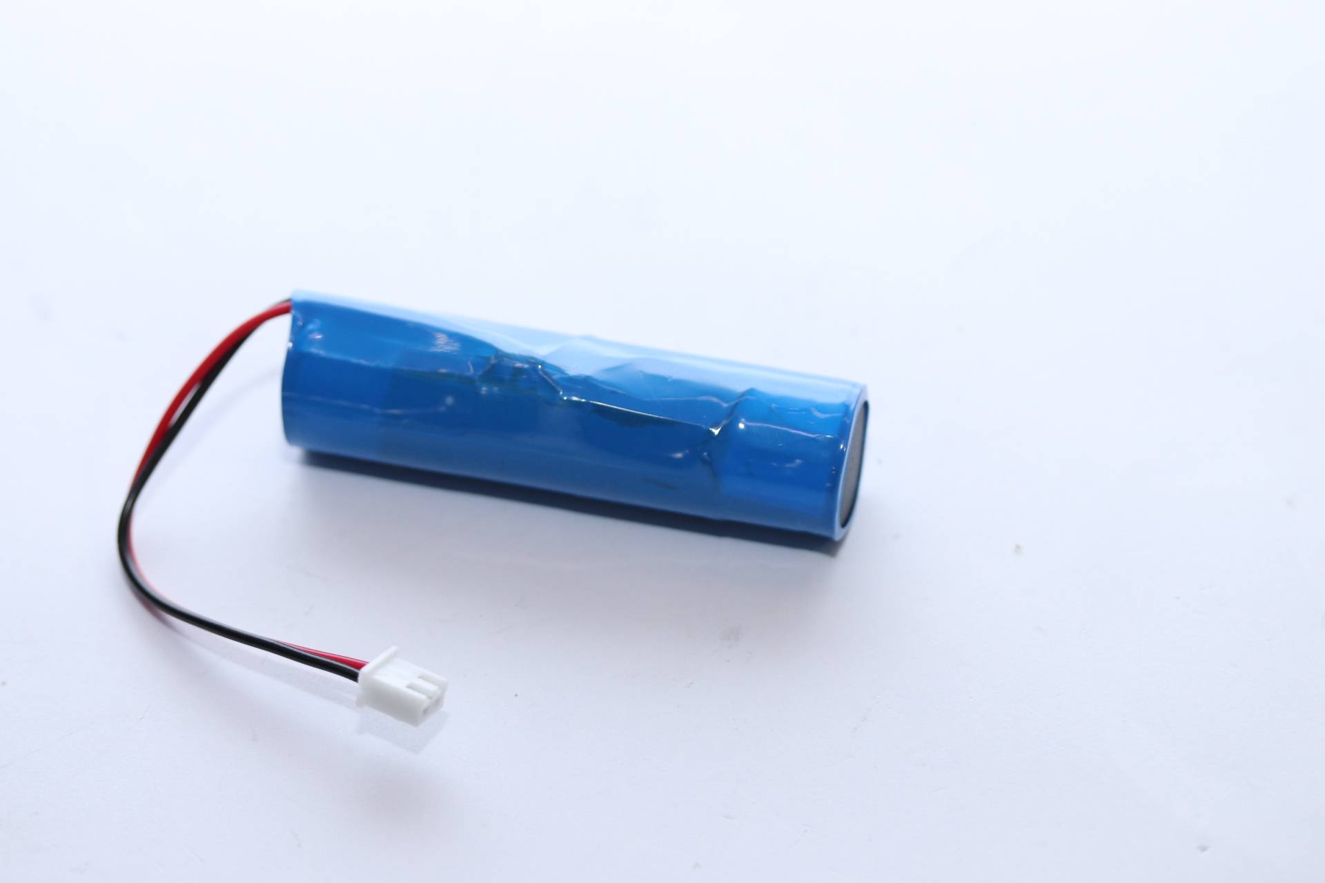 Blauer zylindrischer wiederaufladbarer Batteriepack mit roten und schwarzen Drähten, die an einem weißen Stecker auf weißem Hintergrund enden