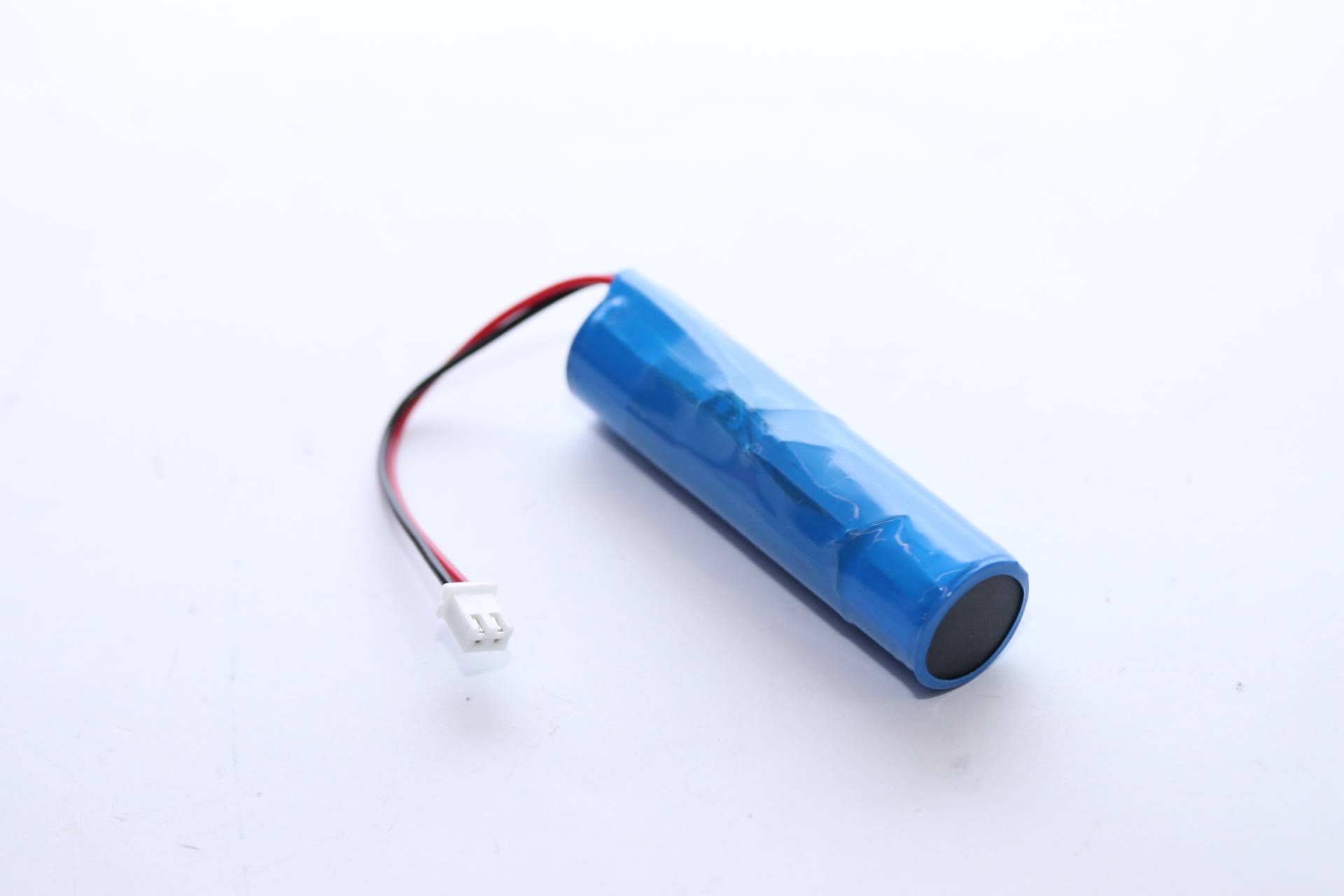 Blauer zylindrischer wiederaufladbarer Batteriepack mit angefügtem rot-schwarzem Kabel und weißem Stecker auf weißem Hintergrund.