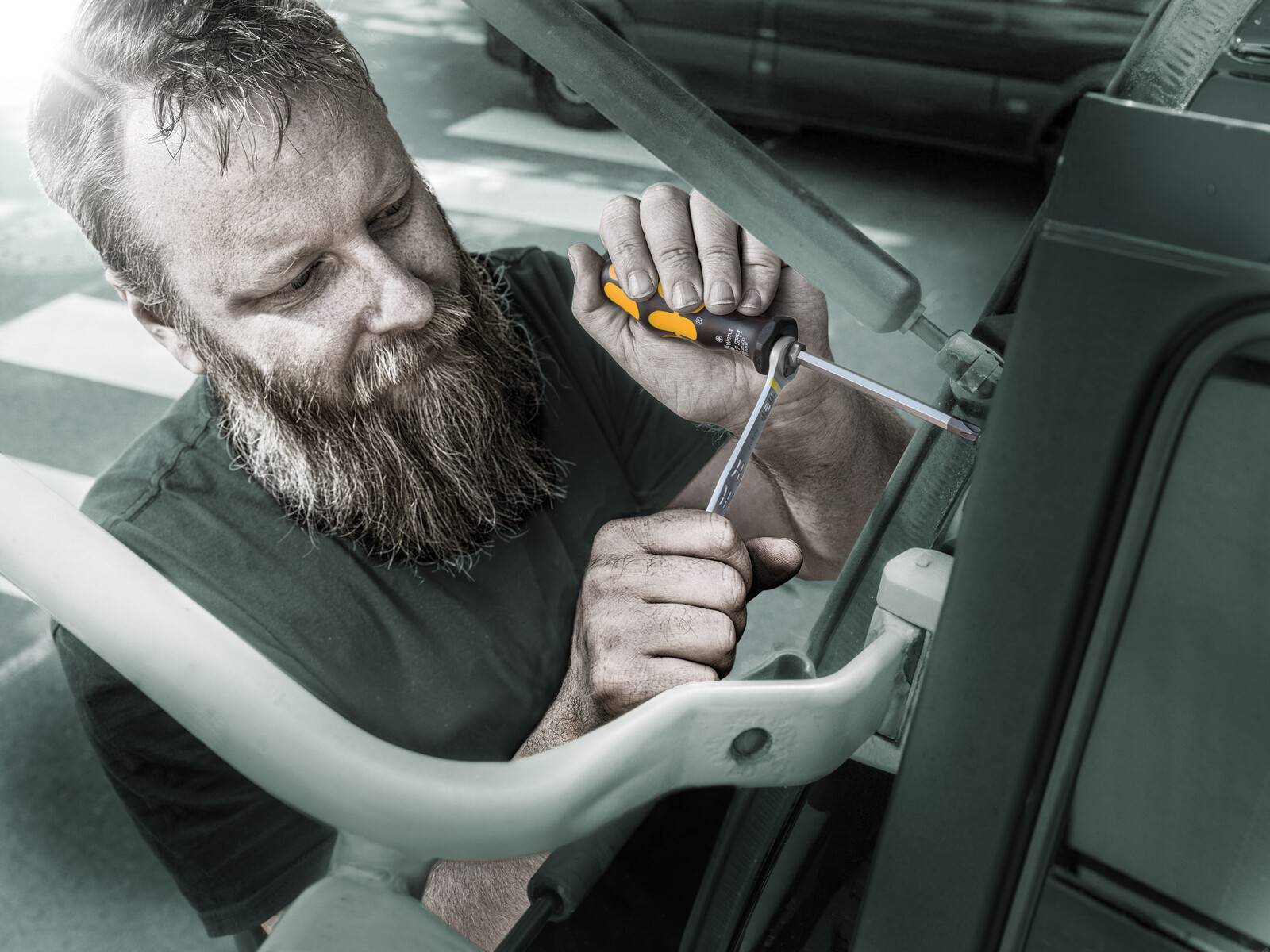 Bärtiger Mechaniker, der einen Schraubendreher verwendet, um einen Fahrzeugfenstermechanismus in einer Autotür zu reparieren.