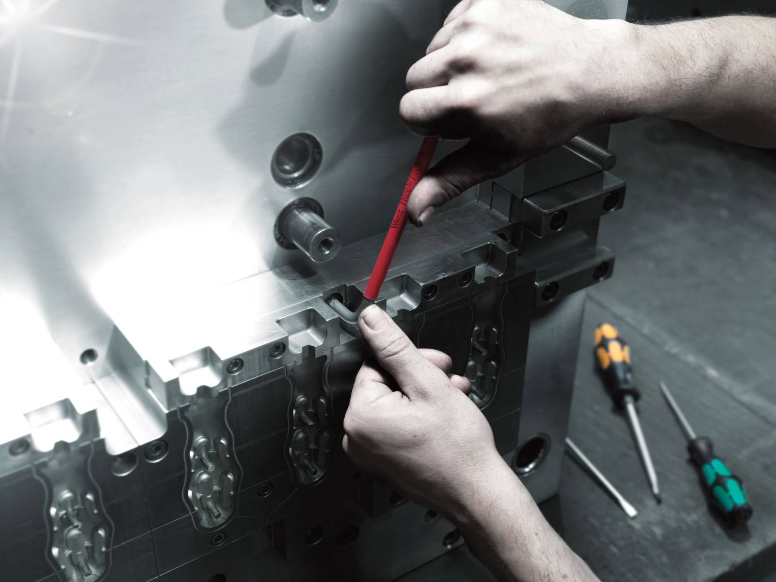 Hände mit einem roten Stift, die ein Metallteil einer Maschine oder eine Form während der industriellen Montage oder Inspektion markieren, mit Schraubenziehern in der Nähe.