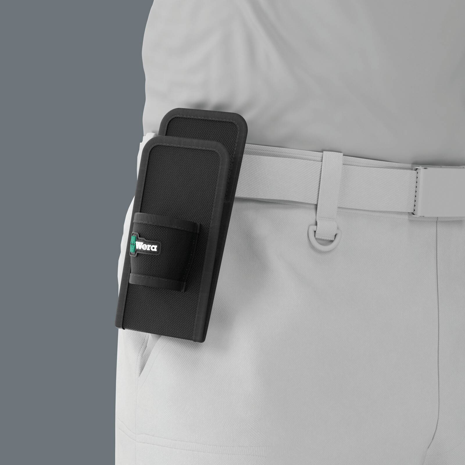 Schwarze Wera-Werkzeugtasche, die an dem Gürtel einer Person befestigt ist, die eine hellgraue Hose vor grauem Hintergrund trägt.