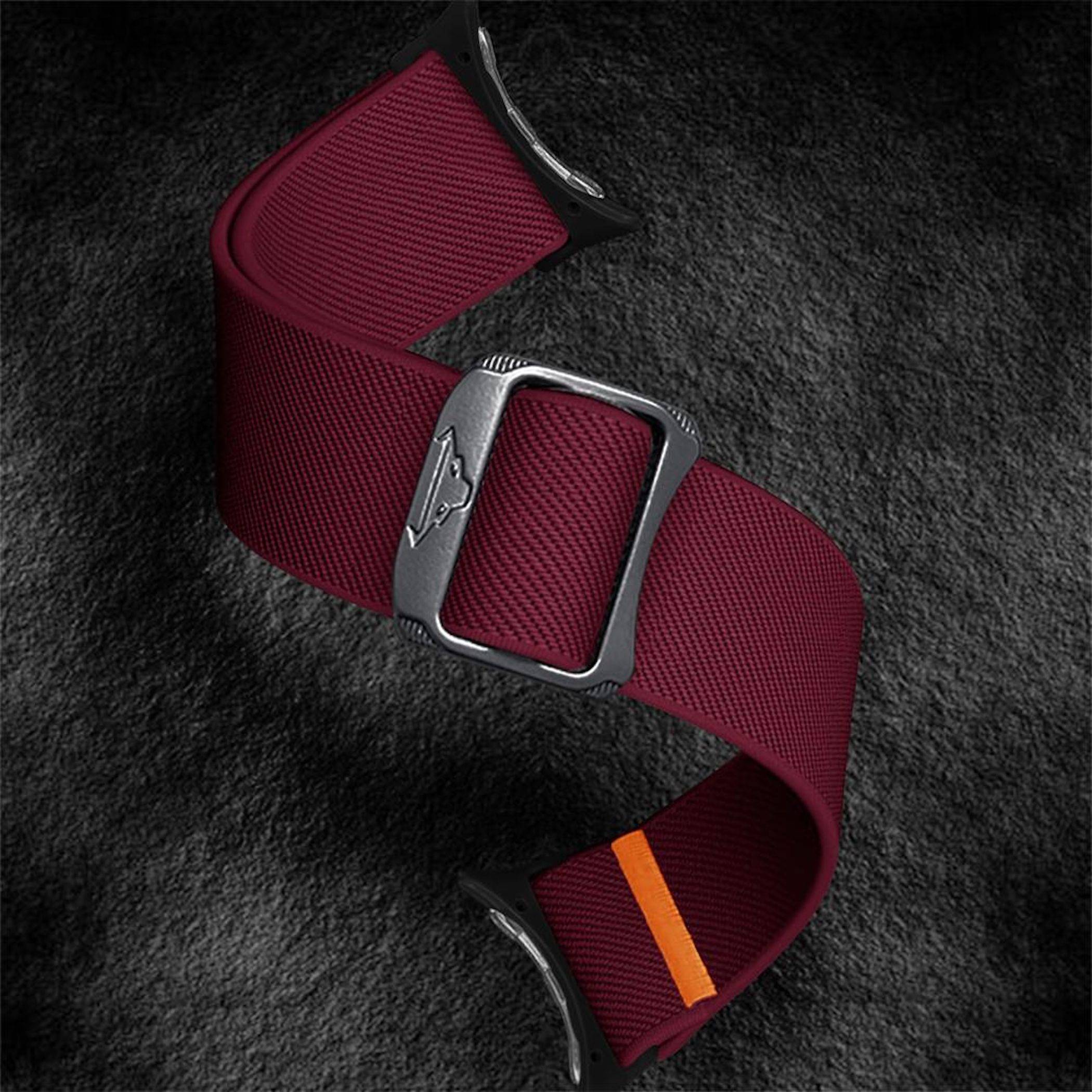 Burgunderrot gewebtes Uhrenarmband mit silberner Schnalle und schwarzer Lederschleife, präsentiert auf dunklem strukturiertem Hintergrund.