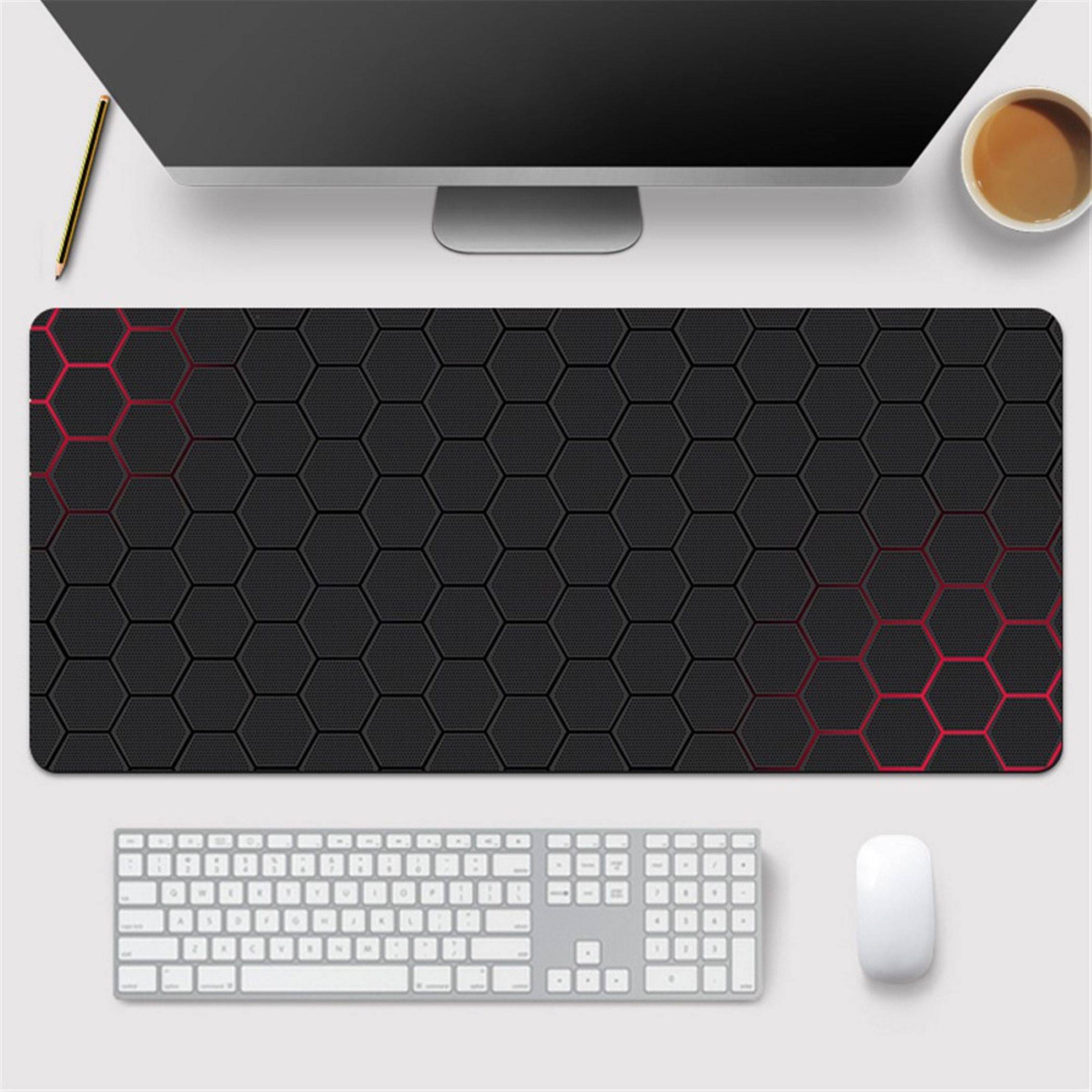 Arbeitsbereich am Desktop mit Monitor, Kaffee, Stift, Tastatur, Maus und einer großen schwarzen Schreibtischmatte mit Sechseckmuster und roten Akzenten.