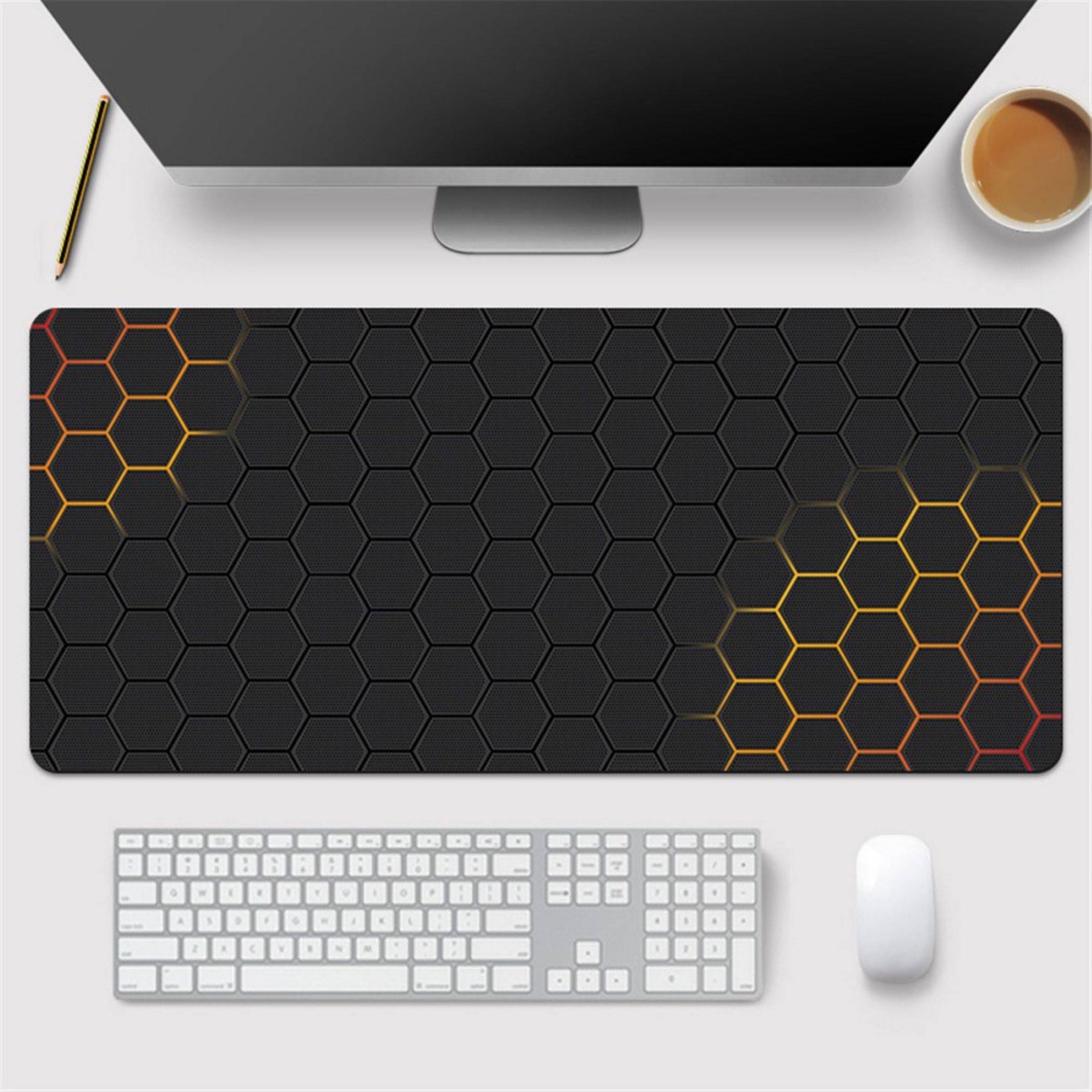 Arbeitsplatz auf dem Schreibtisch mit Monitor, Kaffee, Stift, Tastatur, Maus und einer schwarzen Mousepad mit Hexagon-Muster und orange-gelben Akzenten.