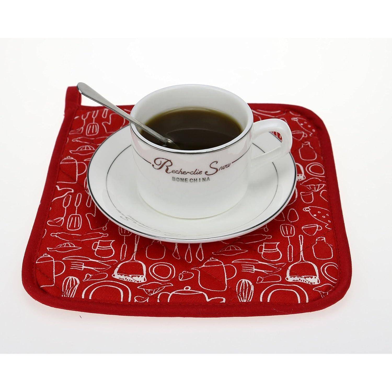 Weiße Kaffeetasse mit Untertasse und Löffel auf einem rot gemusterten Untersetzer, gefüllt mit dunklem Kaffee.