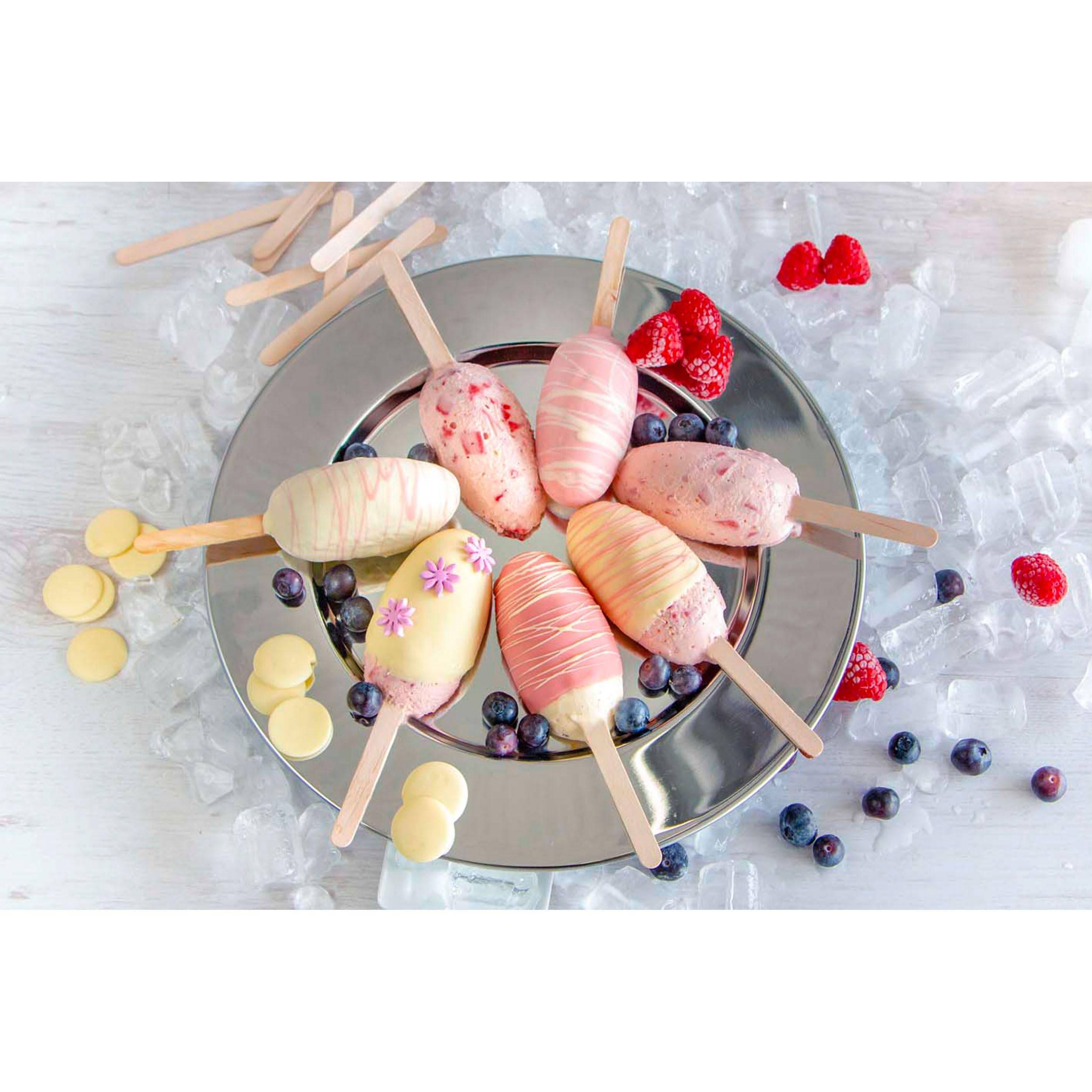 Assortierte Pastelleis-Lollis auf Stielen, arrangiert auf einem Metalltablett über Eis, mit Blaubeeren, Himbeeren und weißen Schokoladenscheiben rundherum.