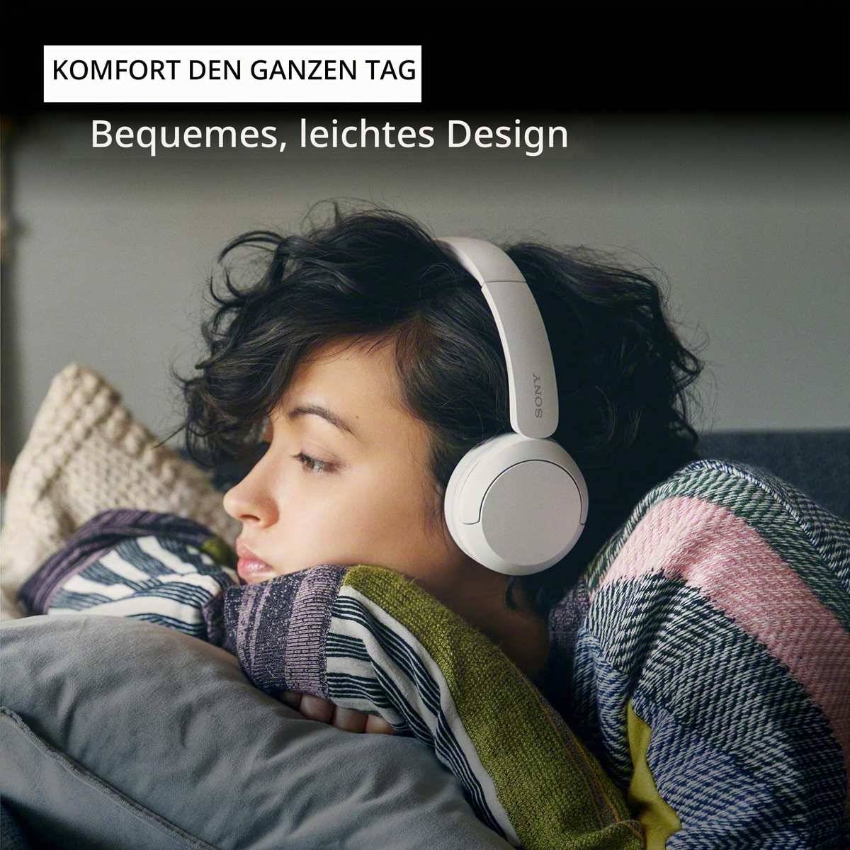 Frau, die auf einem Sofa ruht und weiße Over-Ear-Kopfhörer trägt; der Text lautet „KOMFORT DEN GANZEN TAG