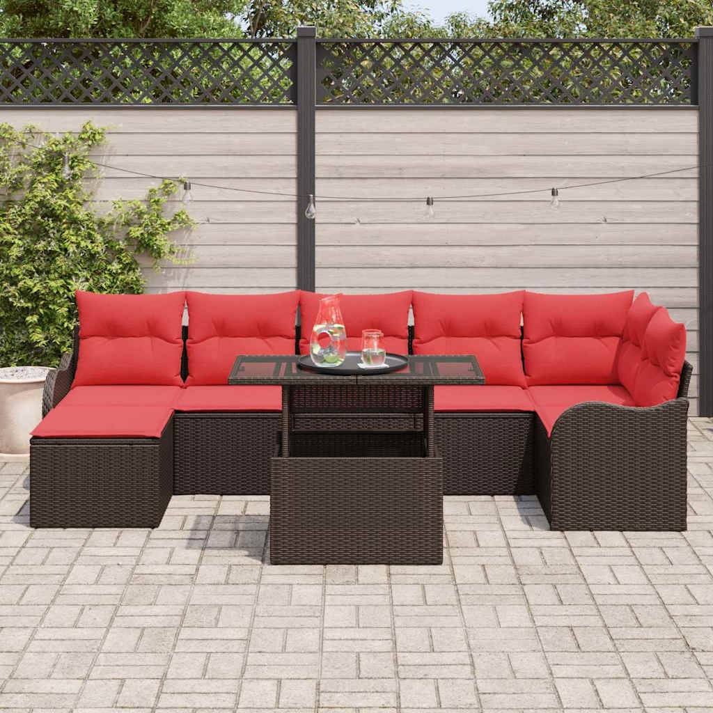 Gartenteeniset mit roten Kissen und dunklem Rattansofa, Ottomane und Glastisch auf einer gepflasterten Terrasse.