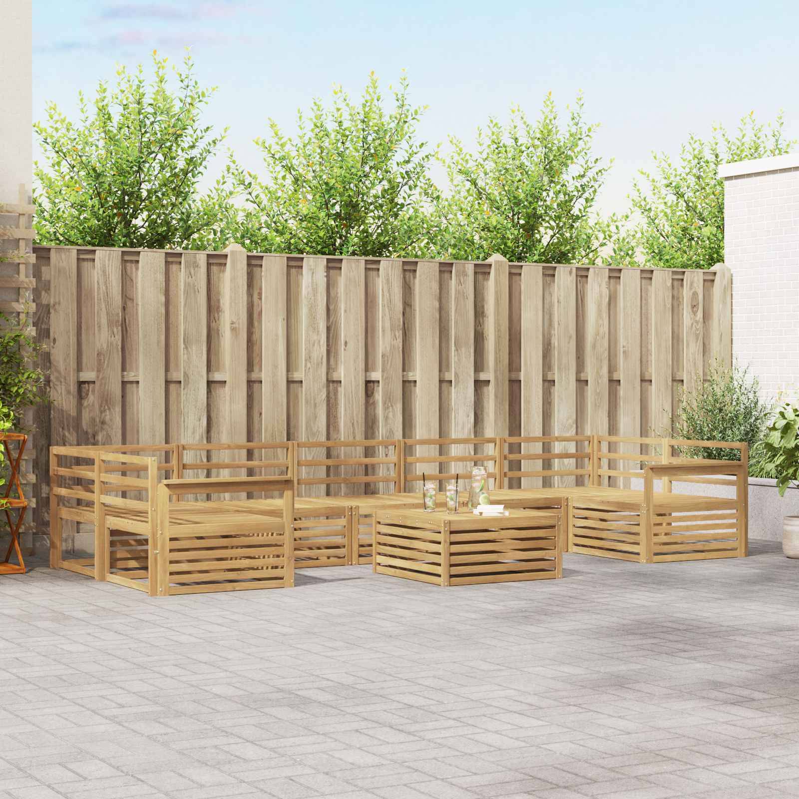 Terrassenbereich im Freien mit Sitzbereiche aus hellem Holz und Couchtisch auf einem gepflasterten Terrassenboden, vor einem Holzzaun und Grünflächen.