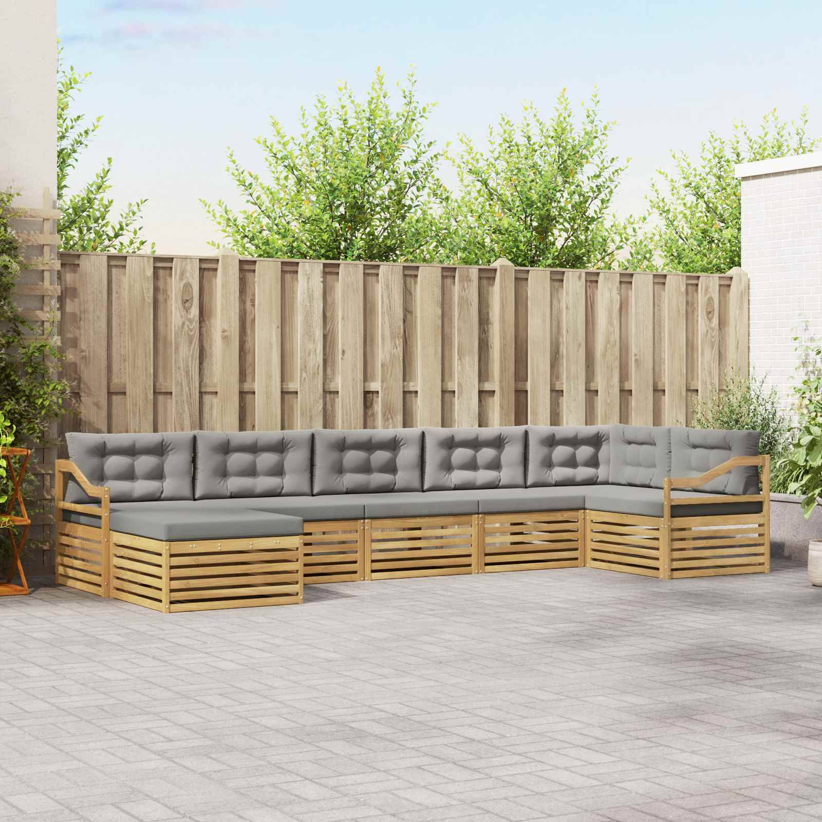 Outdoor L-förmiges Ecksofa mit grauen Kissen und Holzrahmen auf einer Terrasse, vor einem Holzzaun und Grünflächen aufgestellt.