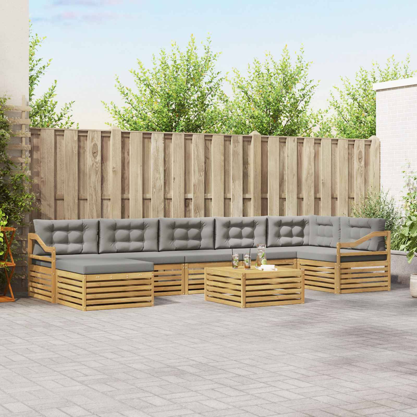 Outdoor-L-förmiges Ecksofa mit grauen Kissen und Holzlattenrahmen um einen niedrigen Couchtisch auf einer Terrasse, im Hintergrund ein Holzzaun.