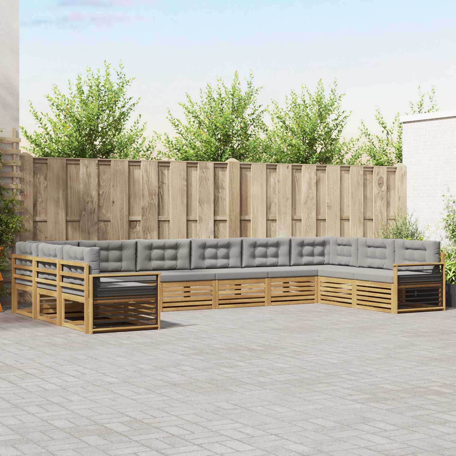 Außenpatio mit einem L-förmigen, grau gepolsterten Ecksofa und passendem Holzrahmen um einen gepflasterten Innenhof, gegen einen Holzzaun und Bäume.