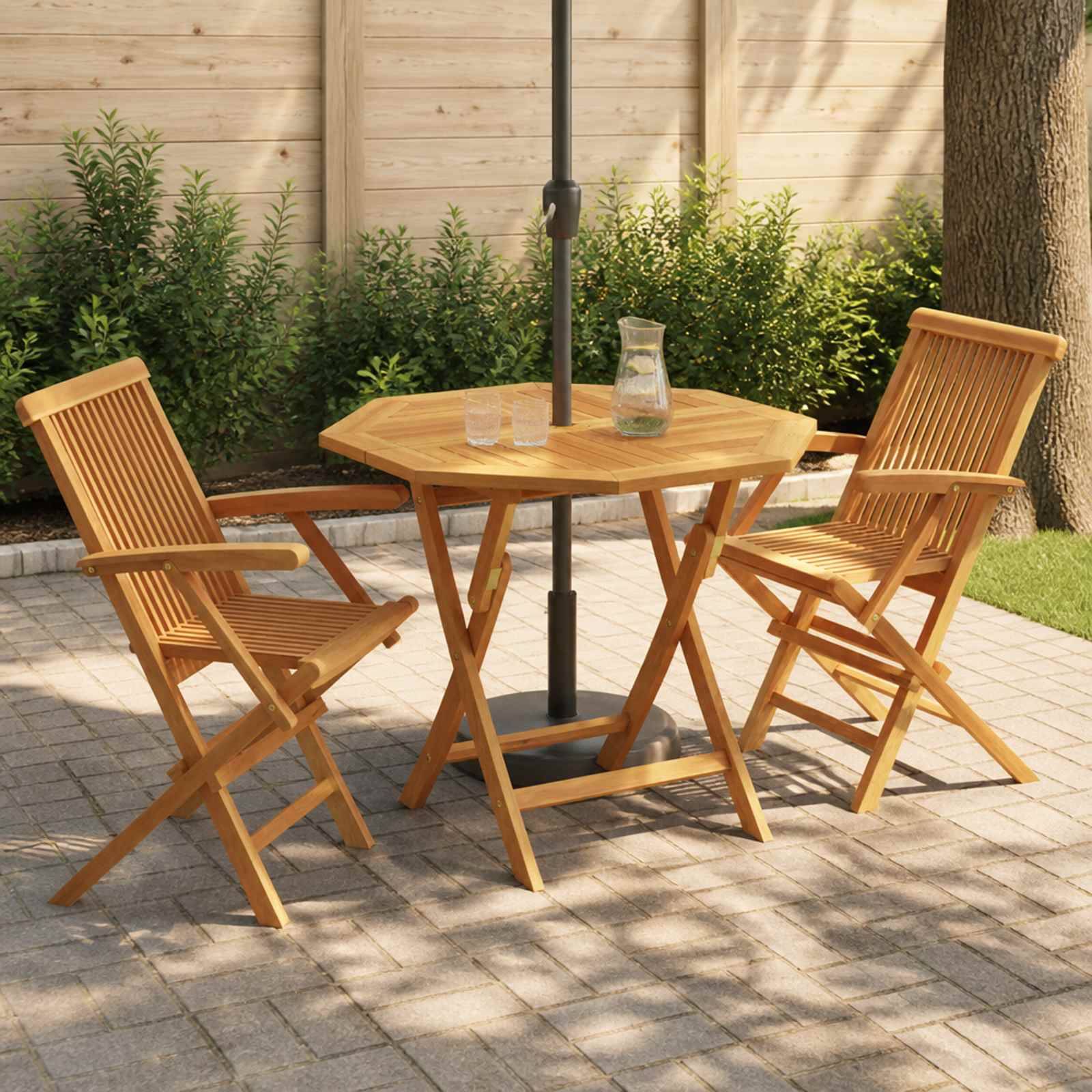 Holzpatio-Tisch mit zwei Klappstühlen unter einem Regenschirm, aufgestellt auf einer gepflasterten Außenterrasse mit einer Karaffe und Gläsern.