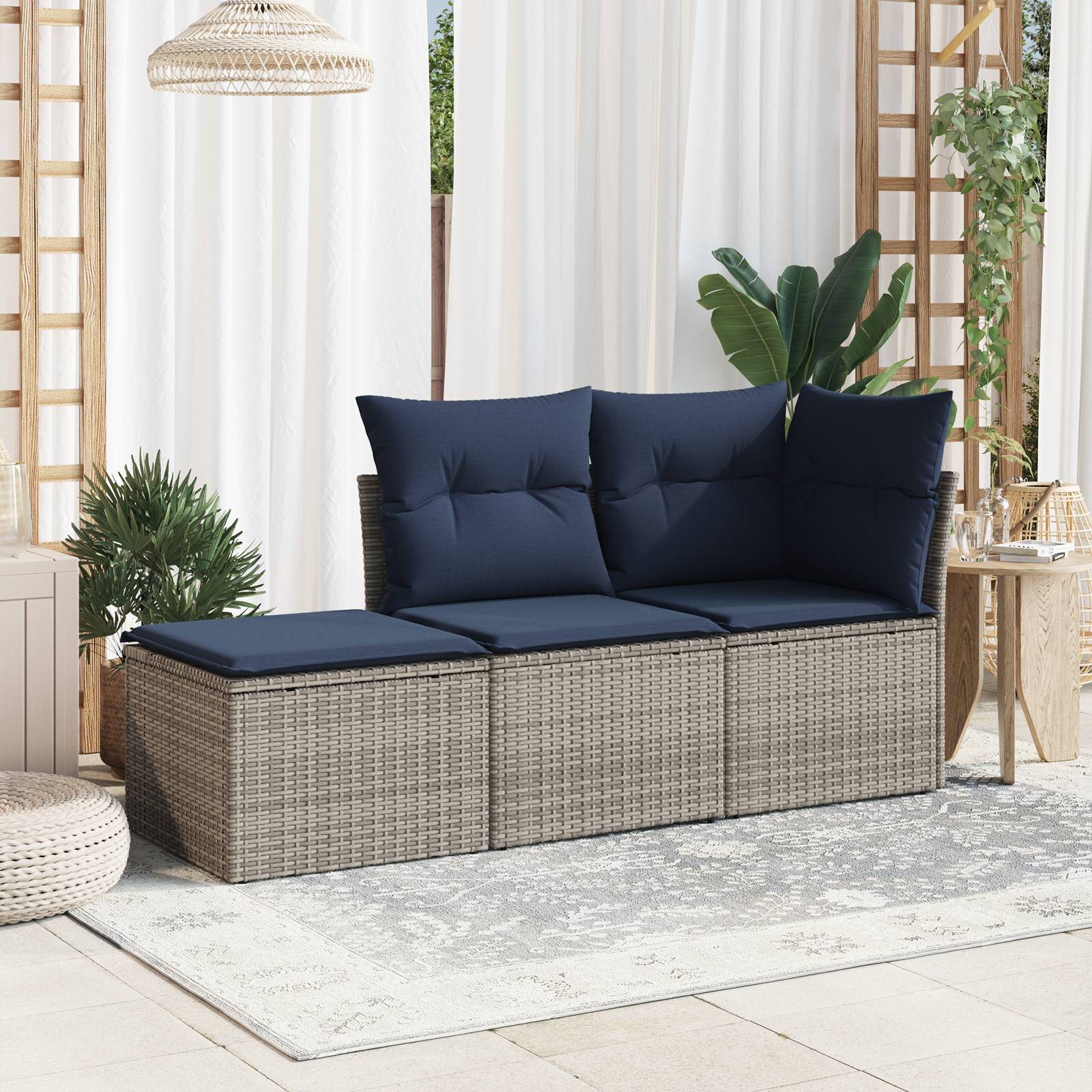 Outdoor-Rattanbank mit marineblauen Kissen und Polstern auf einem hellen Teppich in einer sonnigen Terrassenumgebung mit Pflanzen und Vorhängen.