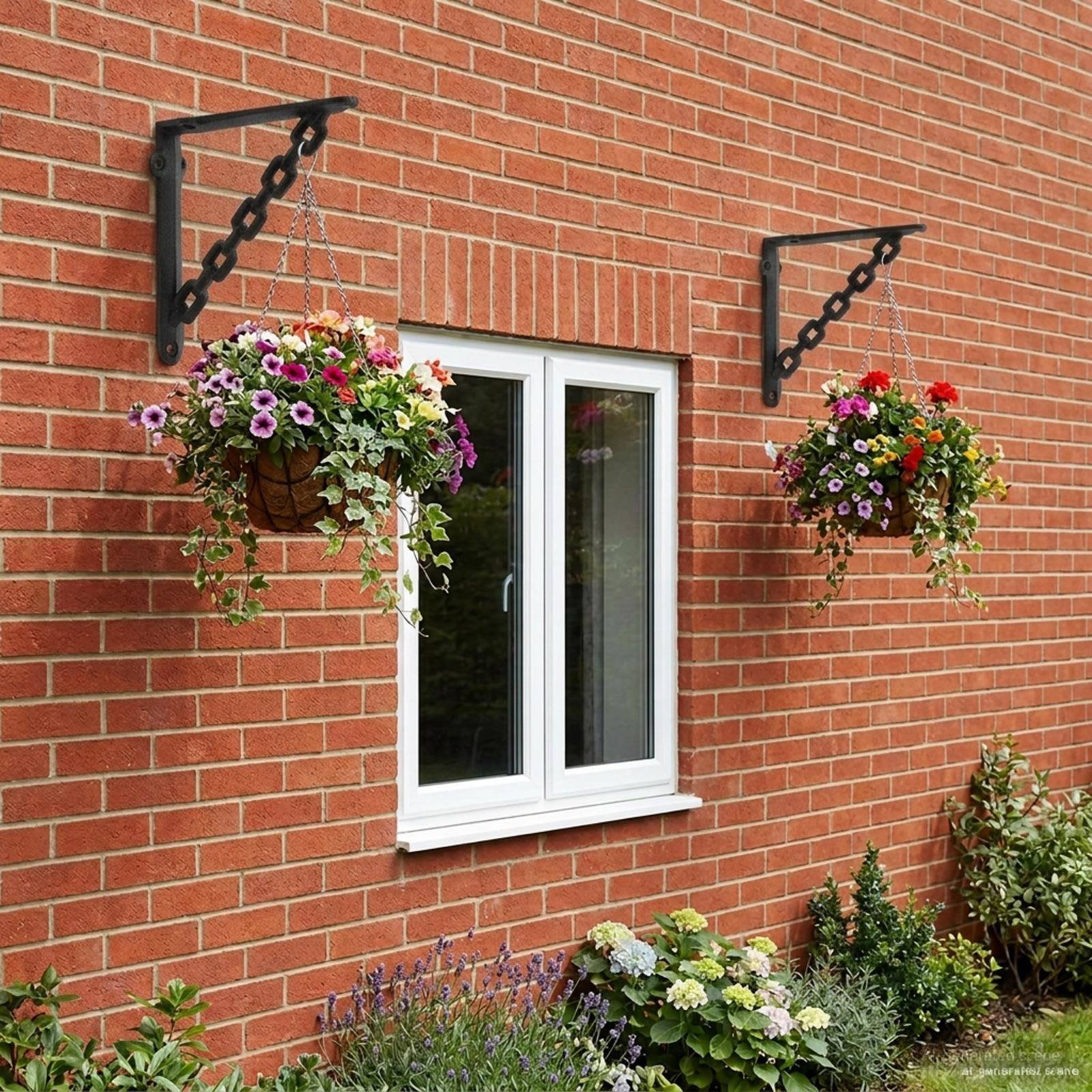 Backsteinhaus-Mauer mit weißem Fenster und zwei hängenden Blumenkörben sowie einem Blumenbeet darunter.