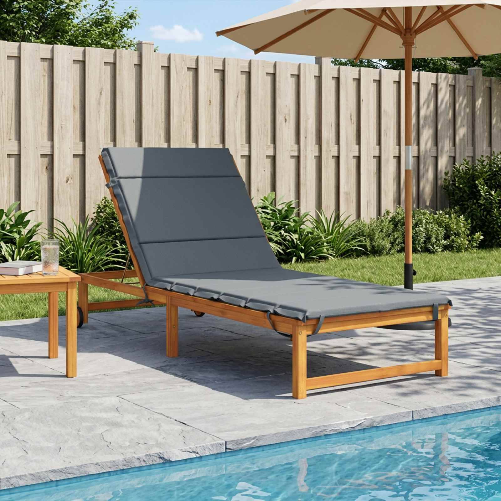 Außenterrasse mit einer grauen gepolsterten Liegeliege neben einem Pool, unter einem Sonnenschirm, neben einem Holzbeistelltisch und Gartenzaun im Hintergrund.